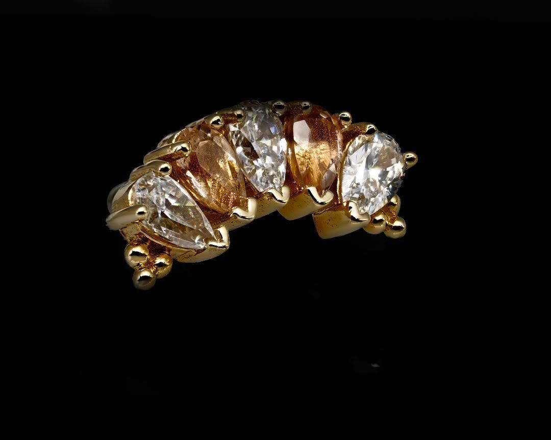 Gold ring with marquise-shaped and round-cut gemstones, set against a black background.