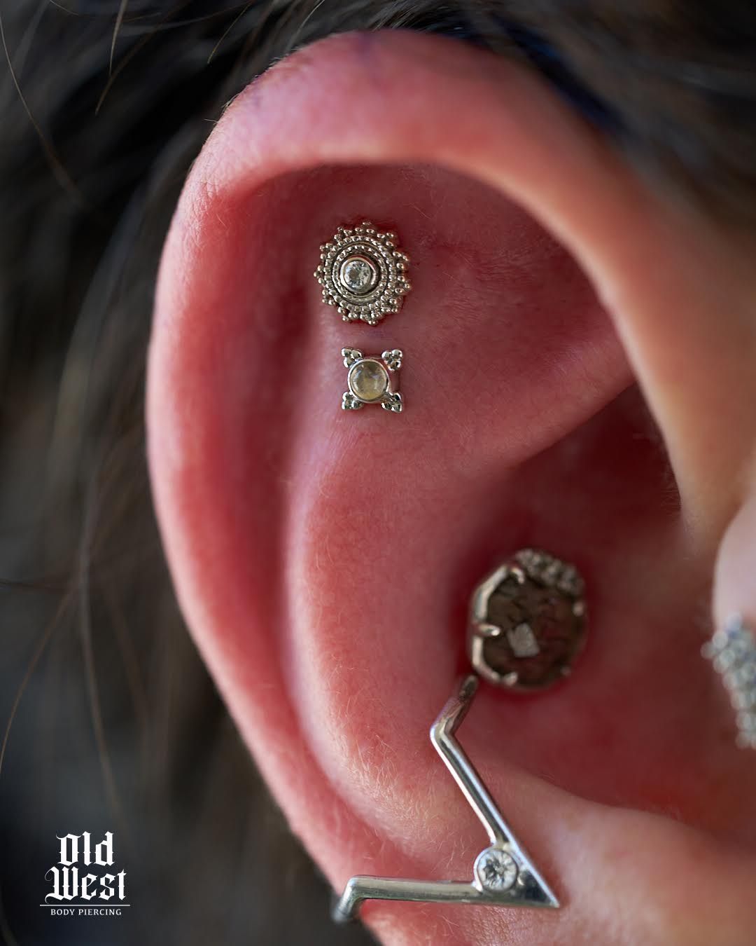 Close-up of ear with three piercings, featuring ornate silver jewelry.