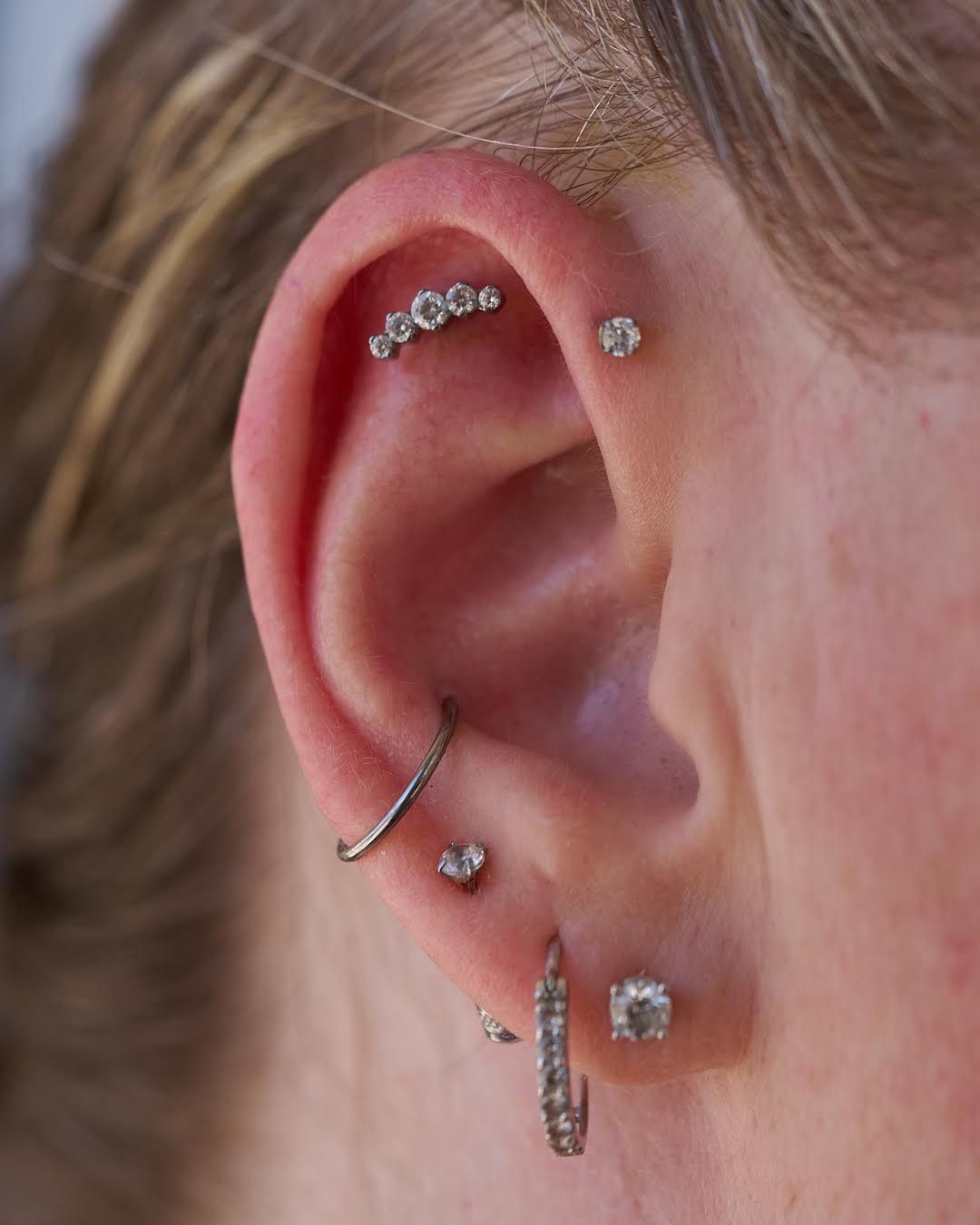 Close-up of ear with multiple piercings, featuring studs and a curved bar of gems.