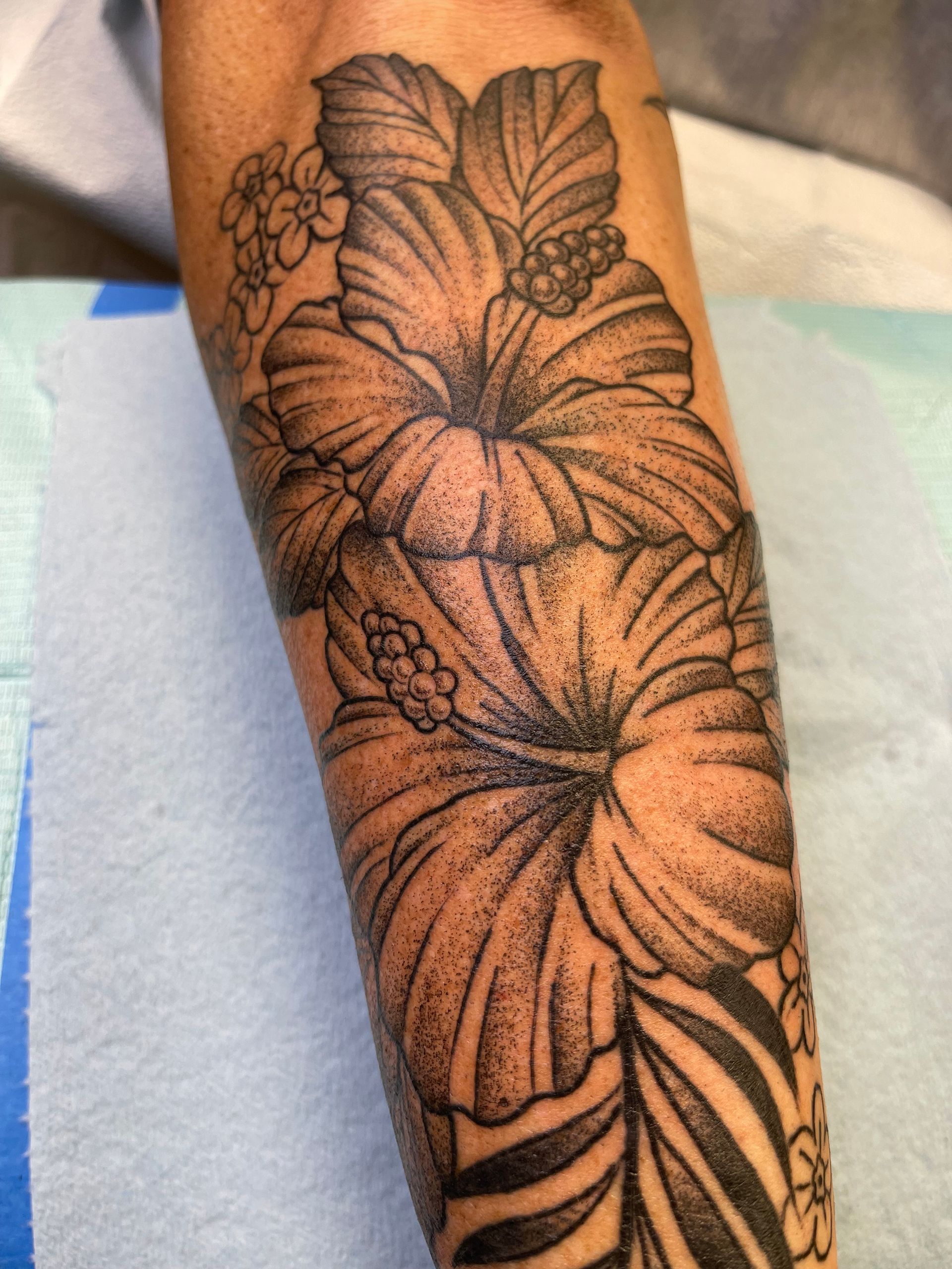 Tattoo of hibiscus flowers with detailed shading on an arm.