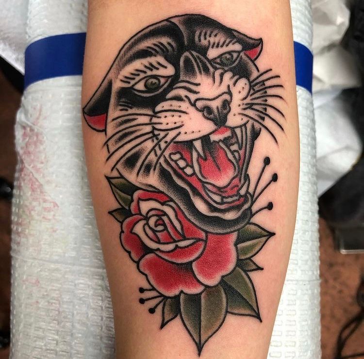 Tattoo of a panther snarling above a red rose; black ink with red and green accents.