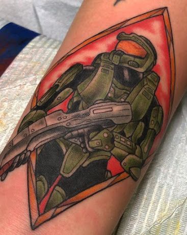 Tattoo of Master Chief from Halo, holding a gun, within a diamond frame, orange and red background.
