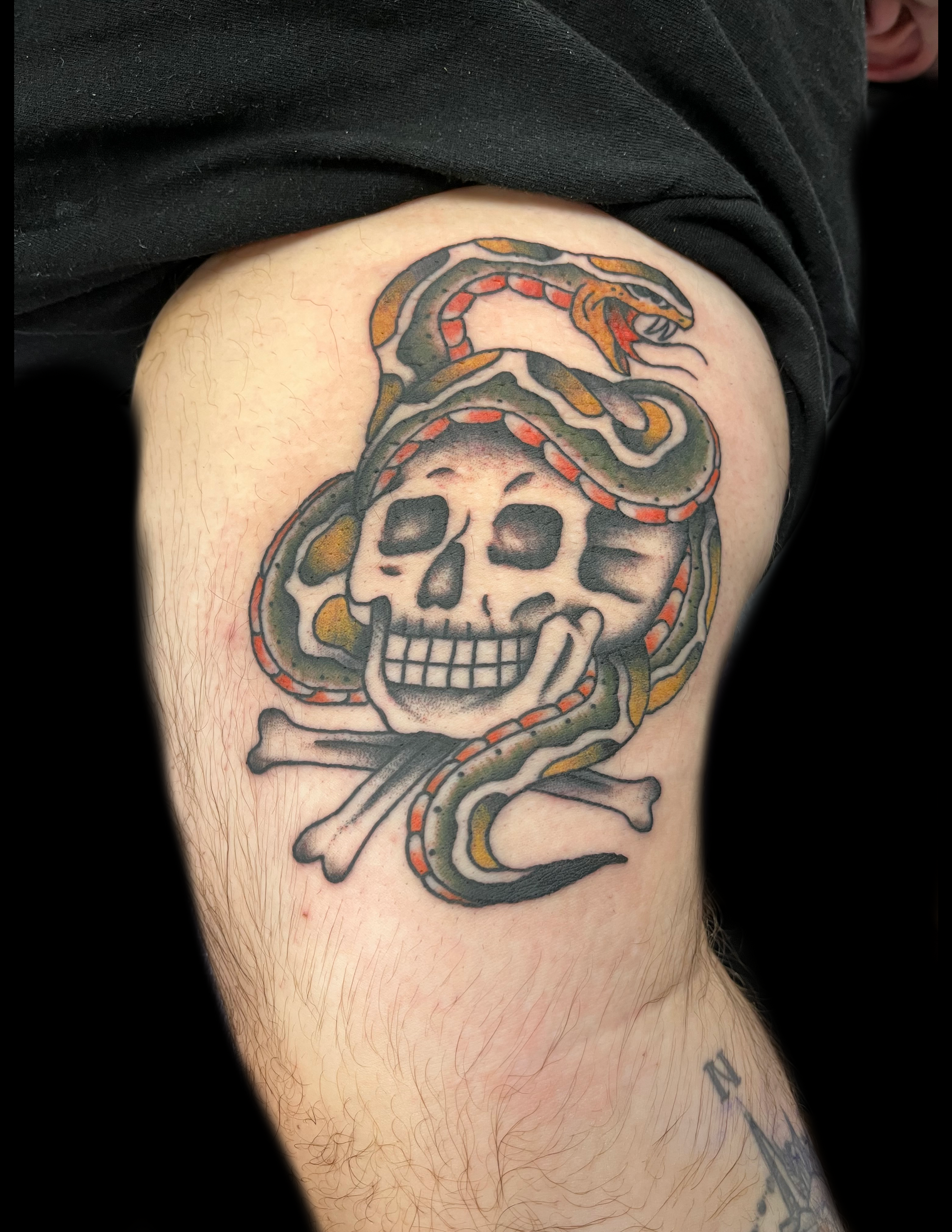 Tattoo of a skull and crossbones with a snake coiled around it, on a person's upper arm.