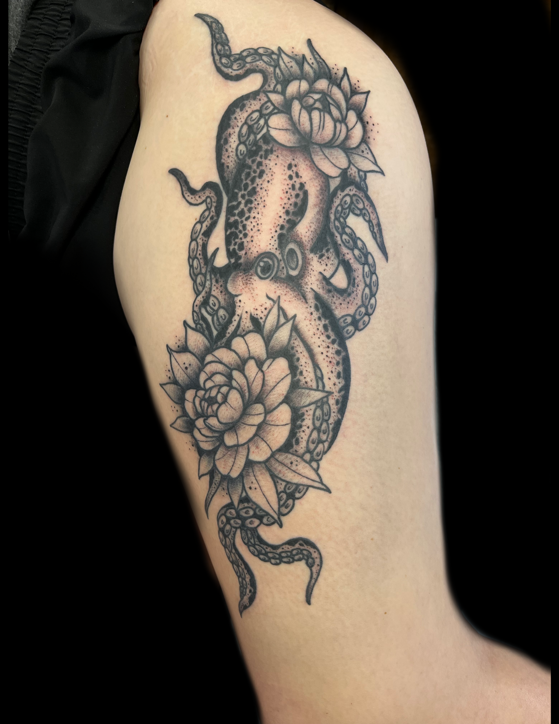 Tattoo of an octopus with two peony flowers on a person's upper arm, in black and gray ink.