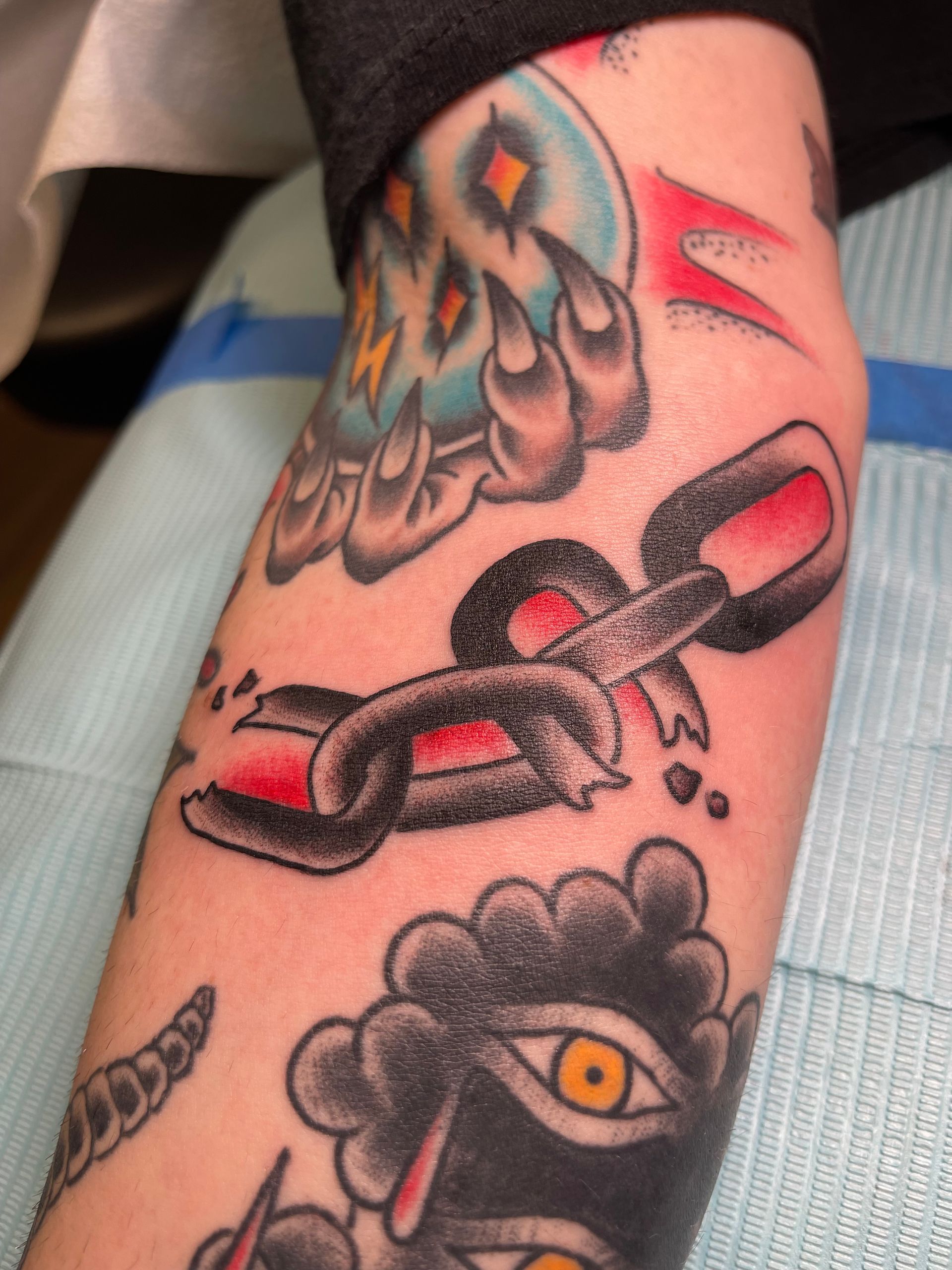 Tattoo of a broken chain with red accents on an arm, with other tattoos visible.
