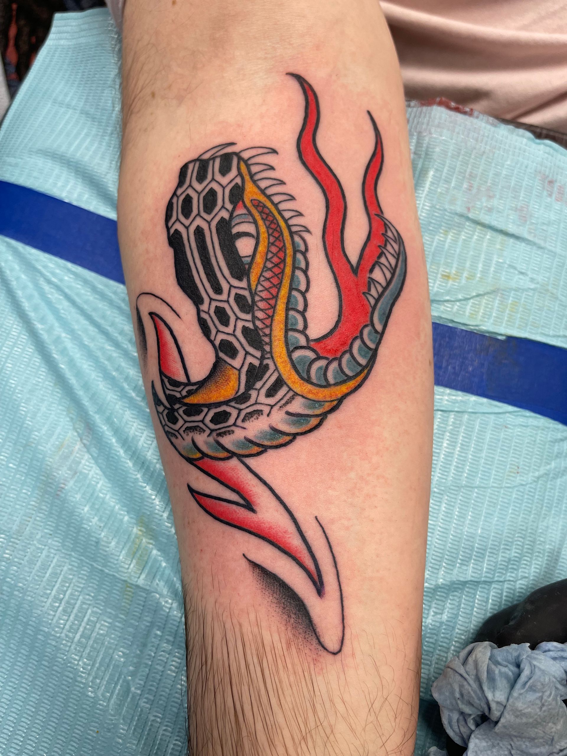 Tattoo of a cobra head with an arrow through it, red and yellow details on forearm.