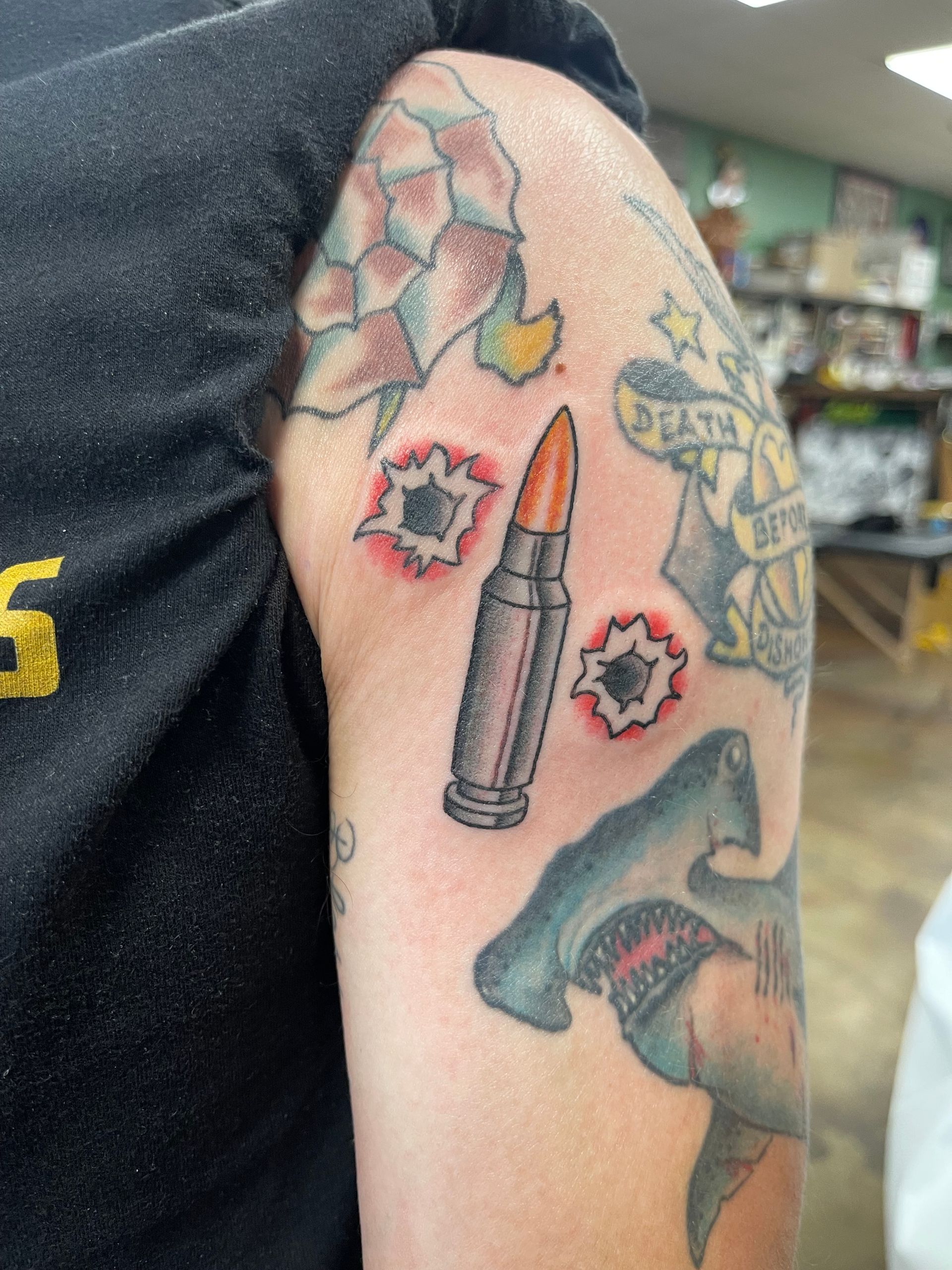 Tattoo on arm, featuring bullet with two bullet holes and other designs.