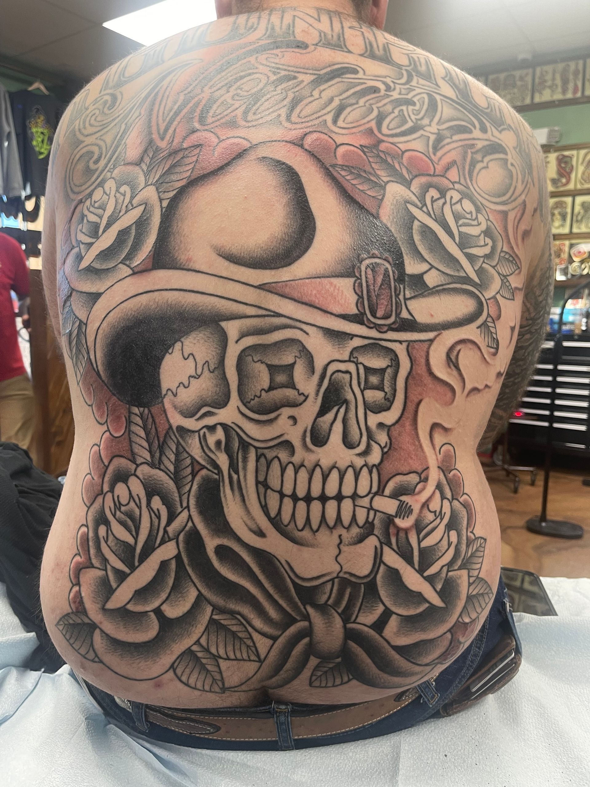 Back tattoo of a skull wearing a hat, surrounded by roses and ornate design.
