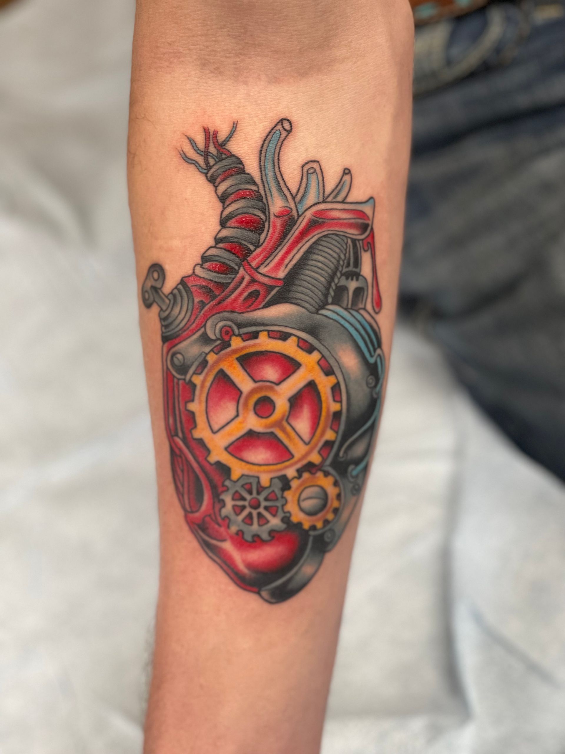 Steampunk anatomical heart tattoo with gears and red, yellow, and gray detailing.