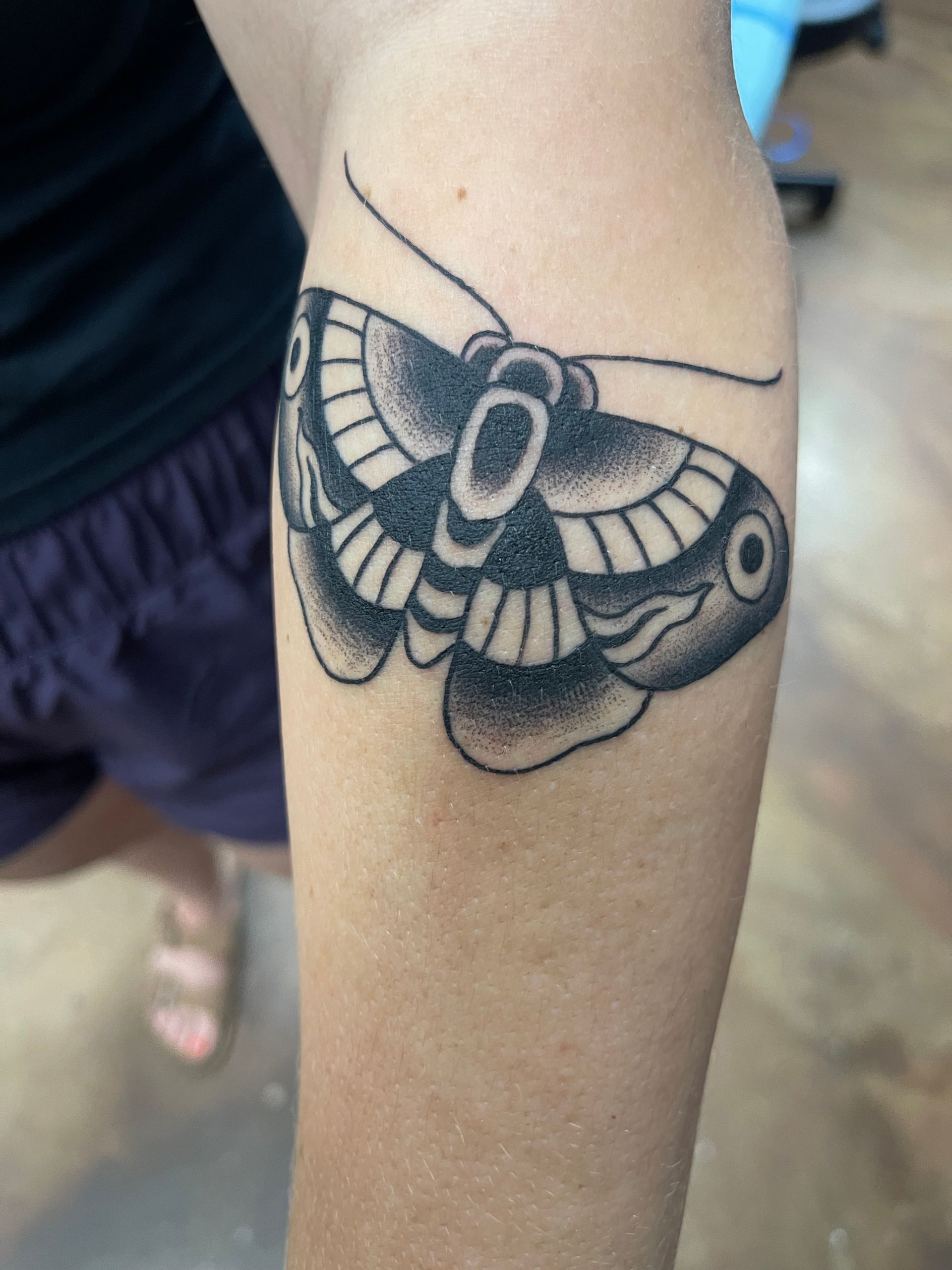 Tattoo of a black and gray moth on a person's forearm.