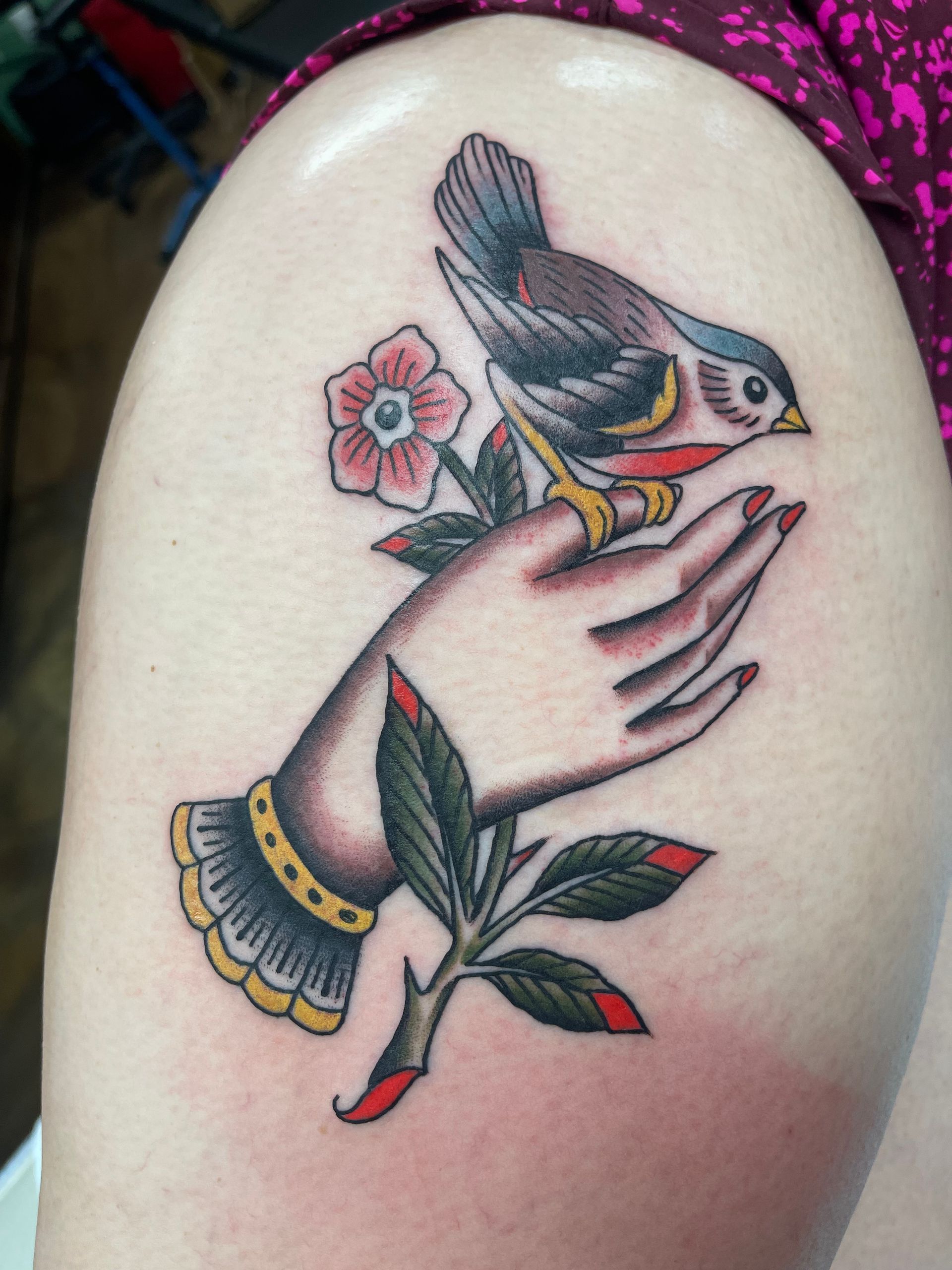 Tattoo of a hand holding a bird perched on a branch with a flower, in traditional style.