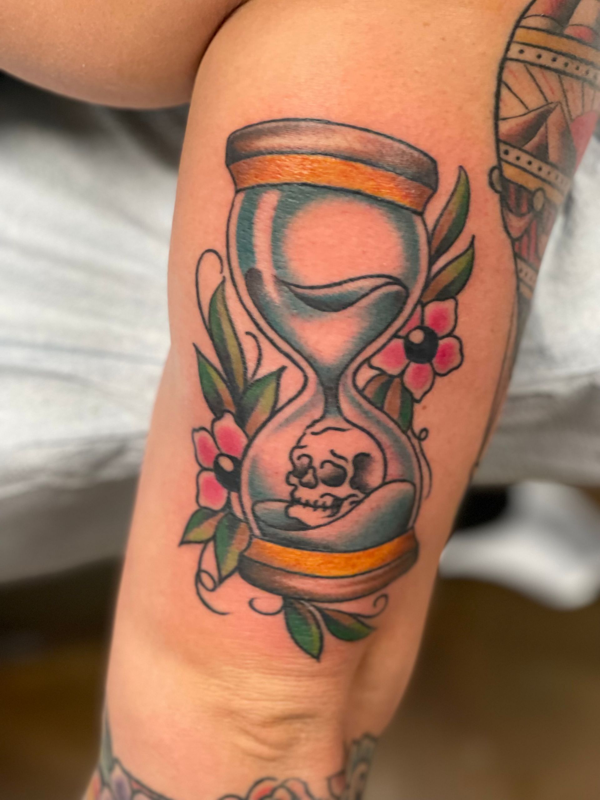 Hourglass tattoo with a skull inside, surrounded by flowers and leaves.