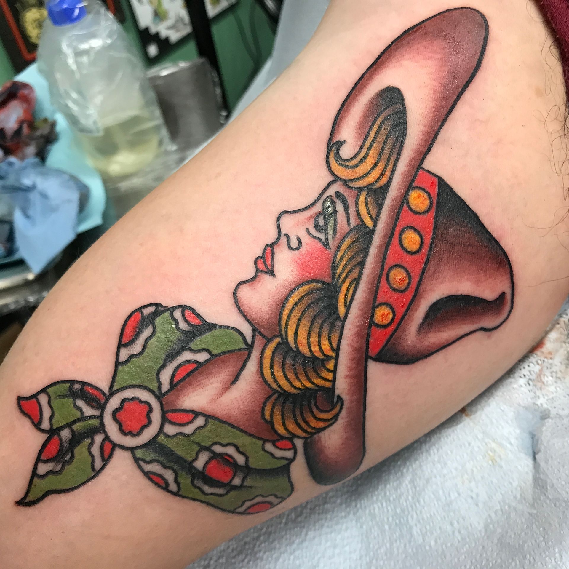 Tattoo of a woman in a cowboy hat and scarf. She looks up with red cheeks. Green and red accents.