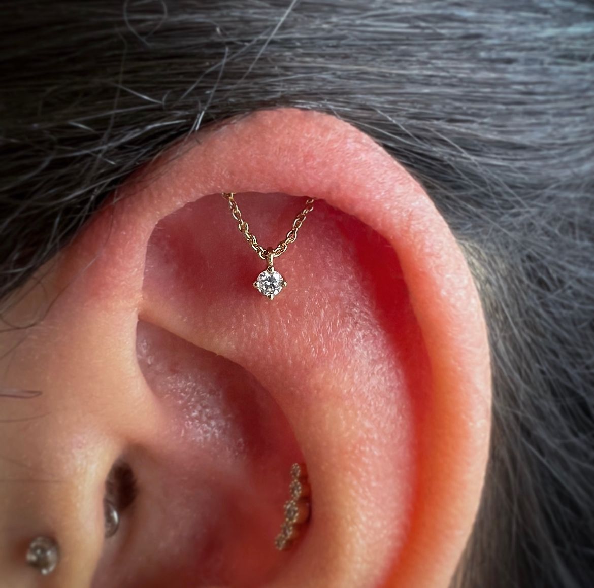 Close-up of an ear with a small gold hoop and dangling stud earring on the upper cartilage.