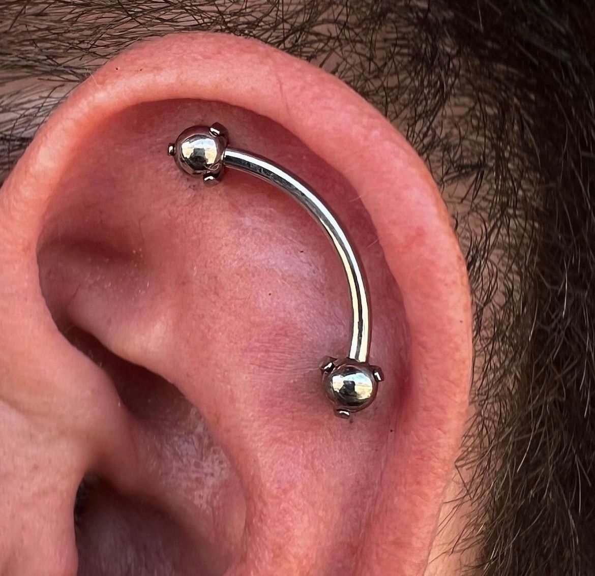 Close-up of an ear with a silver curved barbell piercing on the upper cartilage.