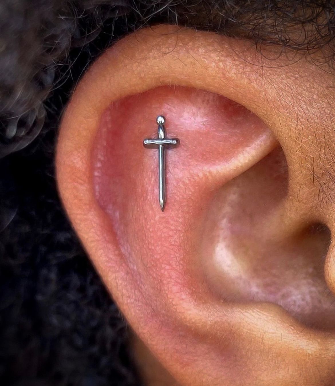 Close-up of an ear with a small silver sword-shaped earring.