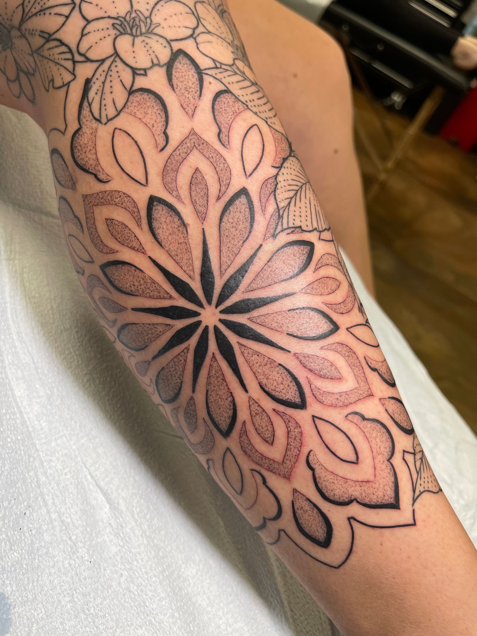 Arm tattoo featuring a dotwork mandala with black and red-brown ink.