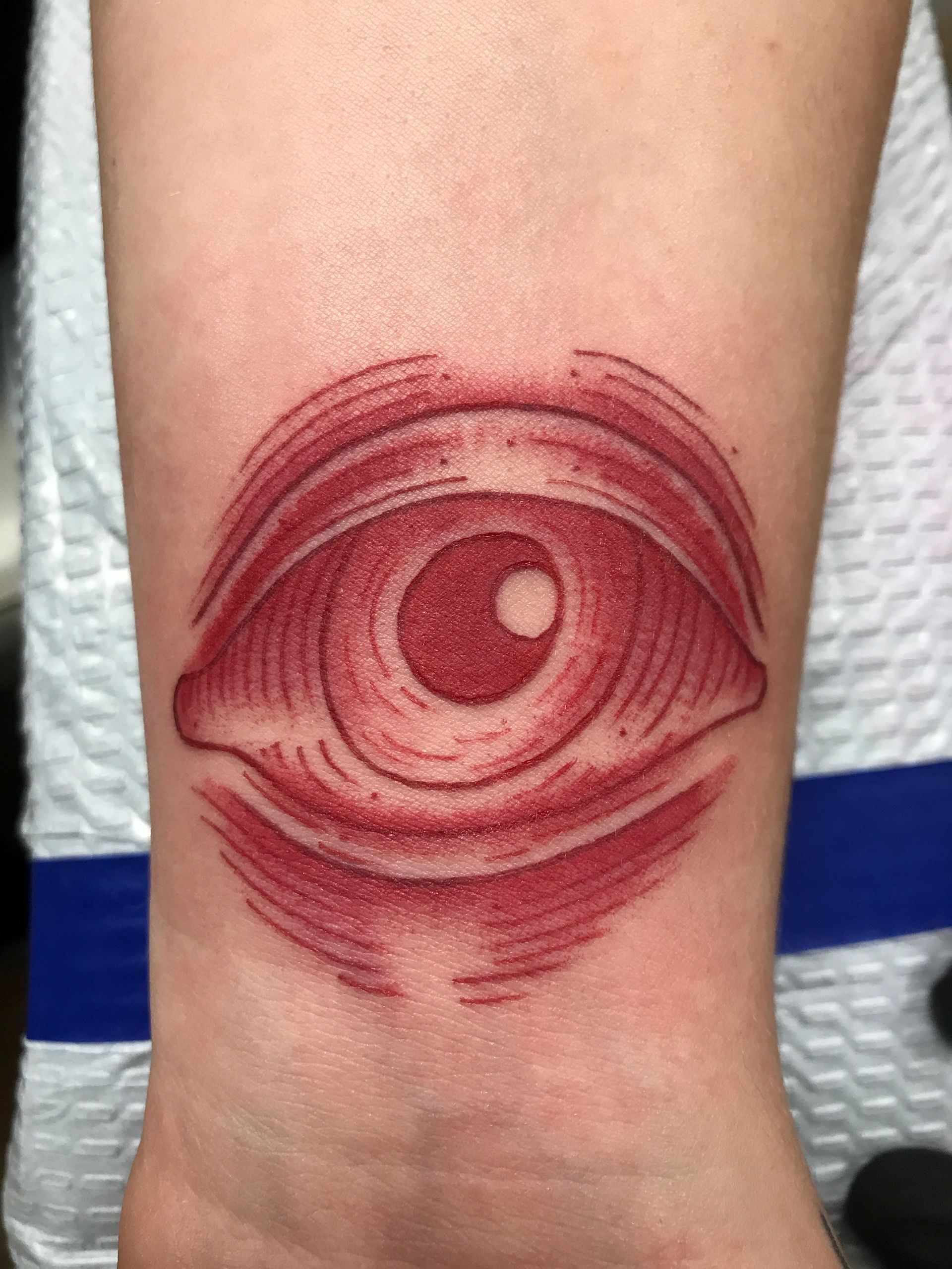 Red, stippled tattoo of an eye on a wrist, with cross-hatching and dot shading.