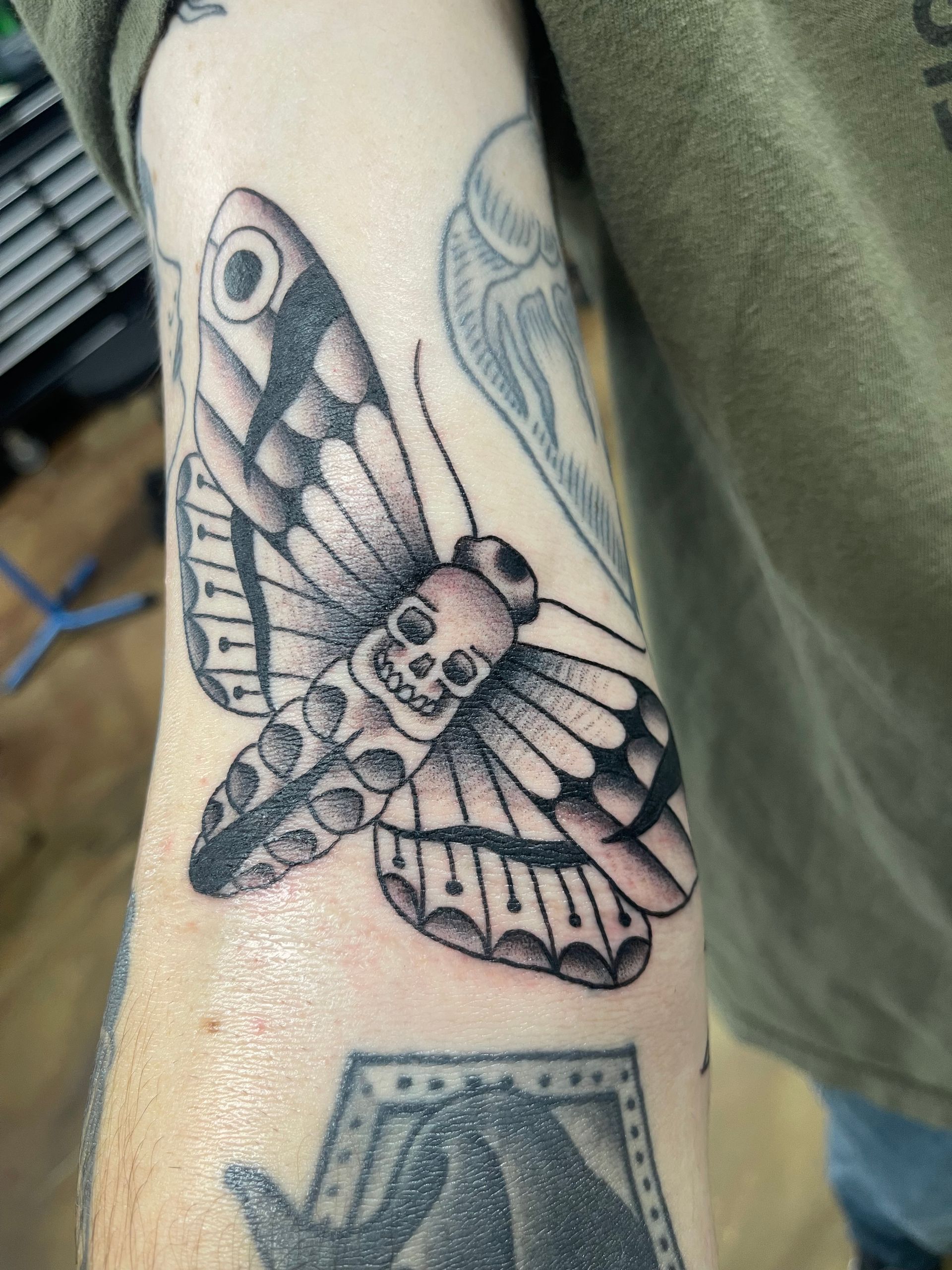 Tattoo of a moth with a skull on its body and detailed wings, on a person's arm.