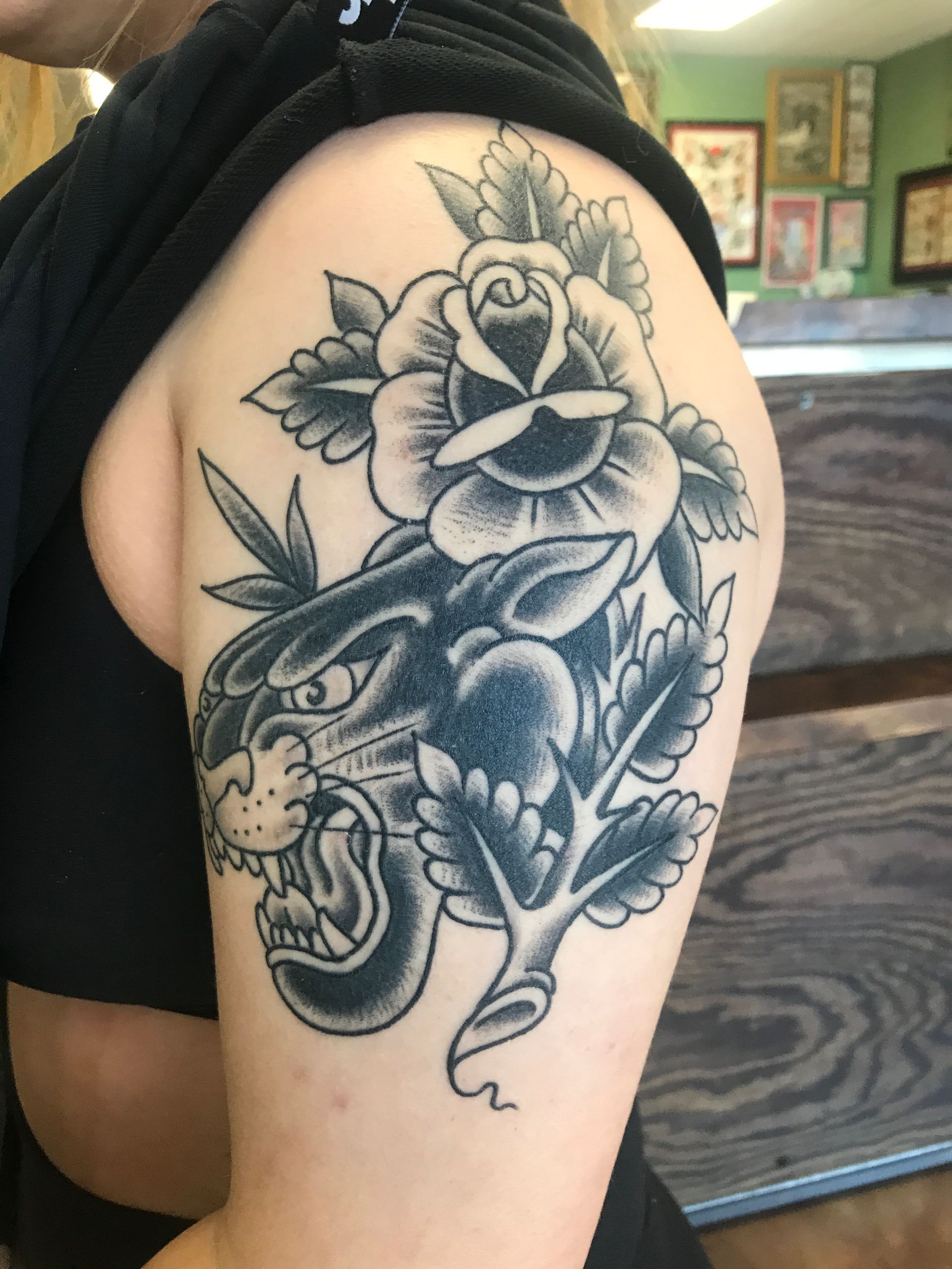 Black panther tattoo with a rose and leaves on a person's upper arm.