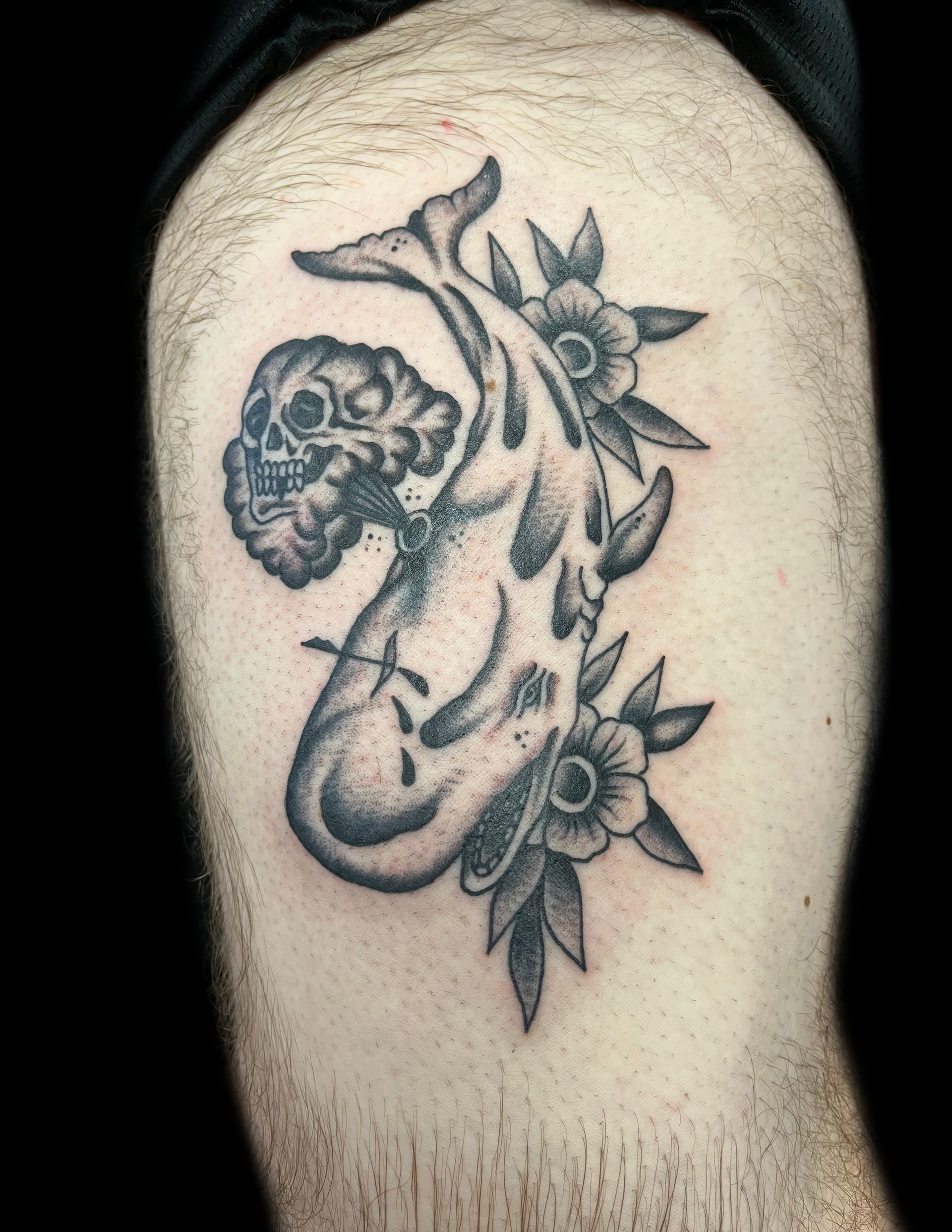 Tattoo of a koi fish with a skull head and flowers, on a person's upper arm. Black and white.