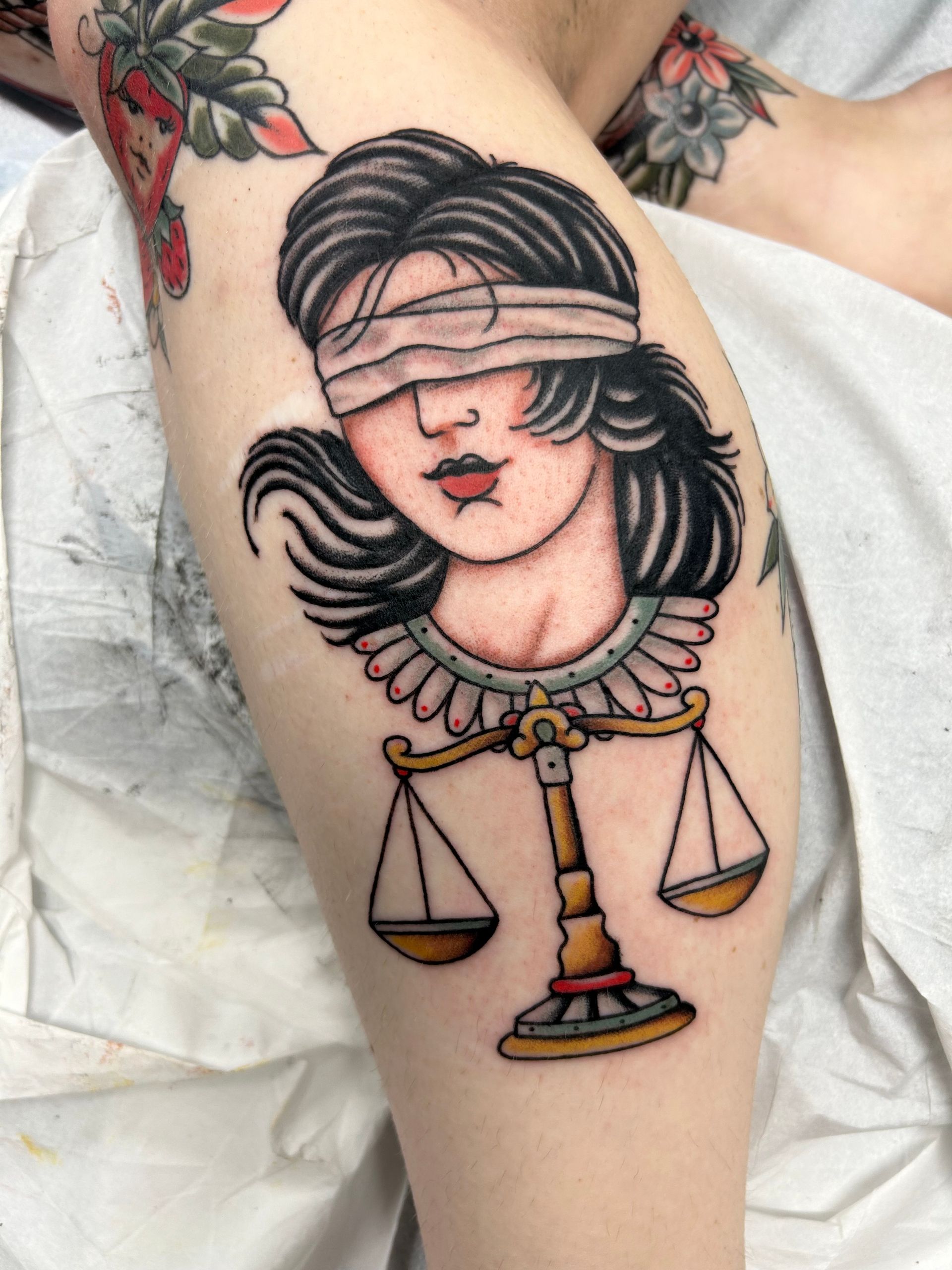 Blindfolded woman with scales tattoo, black hair, on leg, with colorful details.