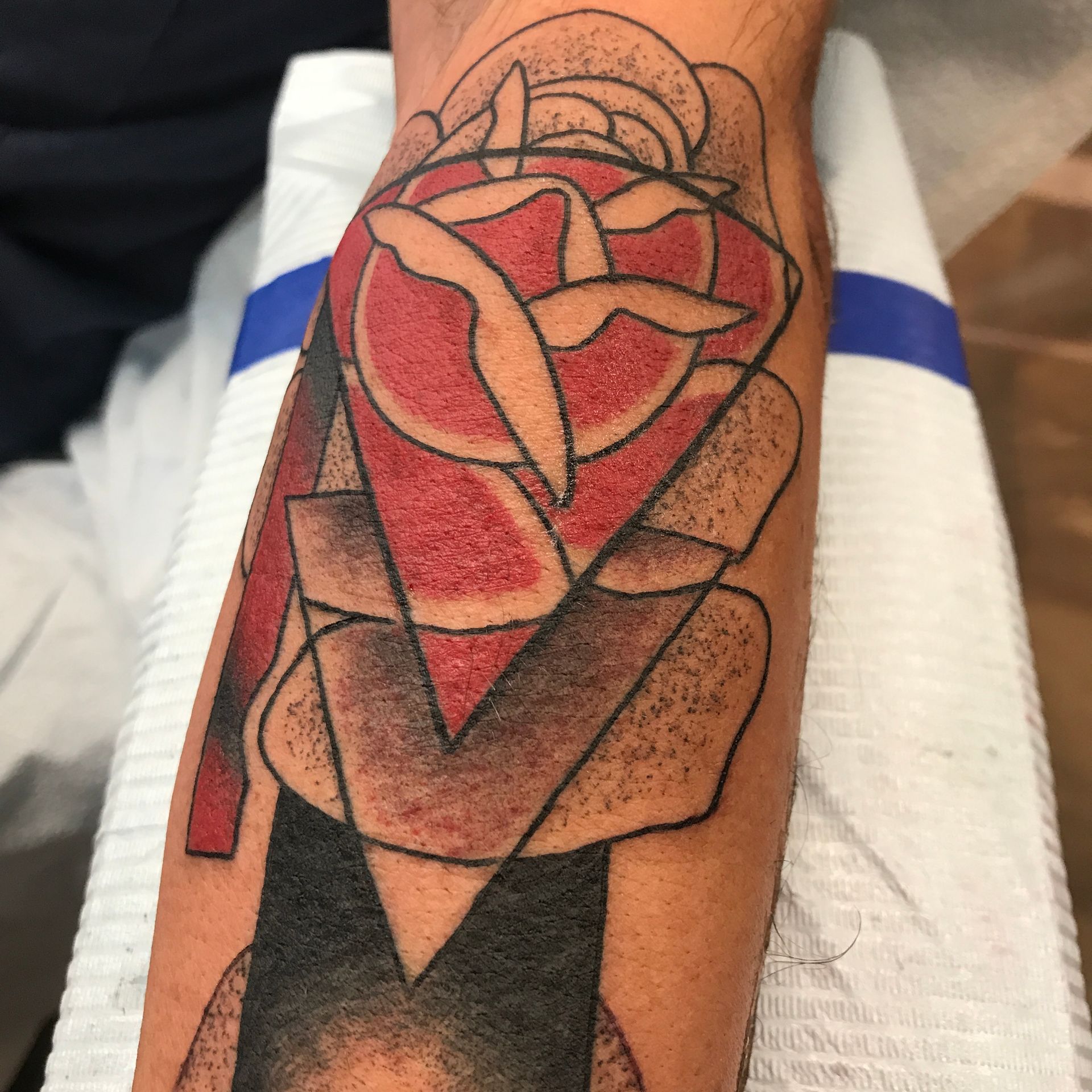 Tattoo of a geometric rose in red, black, and beige on a forearm.