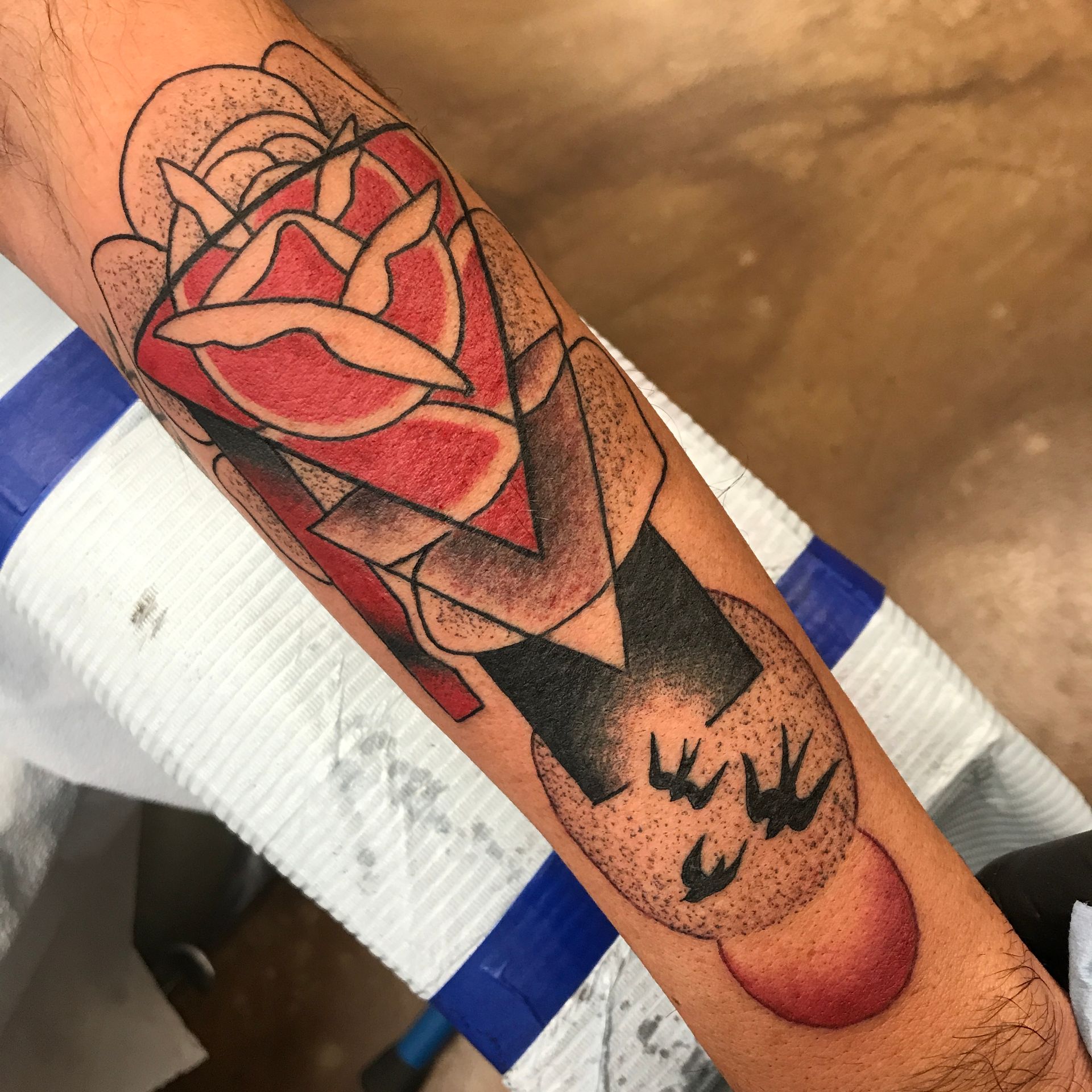 Tattoo of a red rose with black geometric shapes and swallows on an arm.