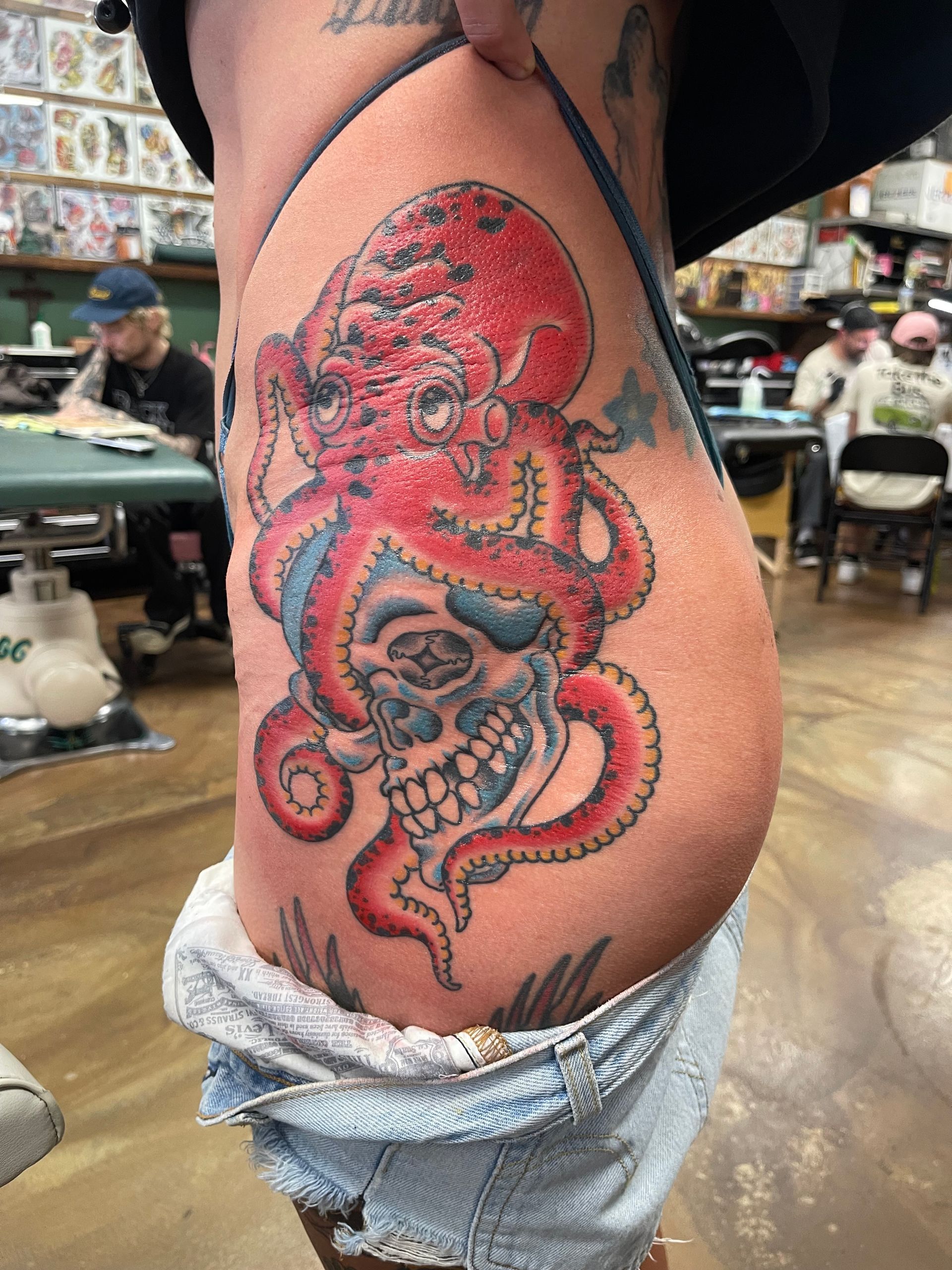 Tattoo of a red octopus over a skull, on a person’s side. In a tattoo parlor setting.