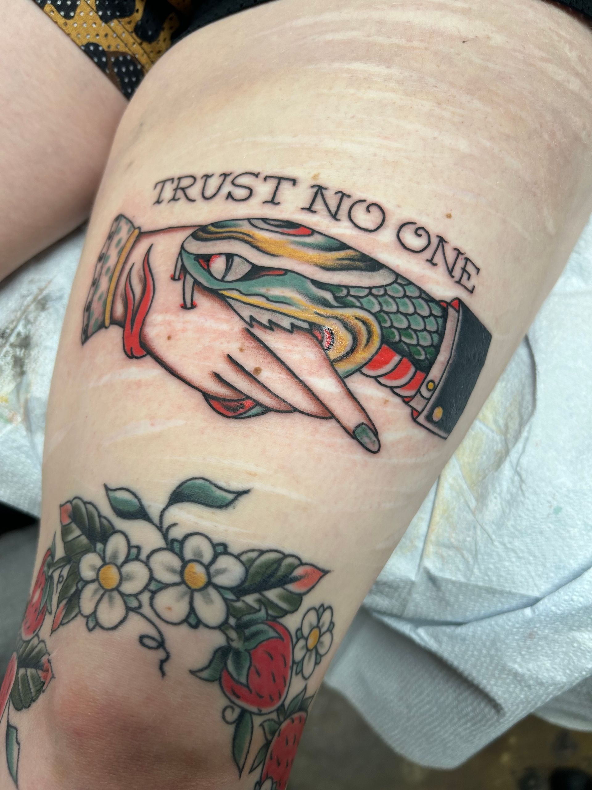 Tattoo on a leg: Handshake with snake head, text 