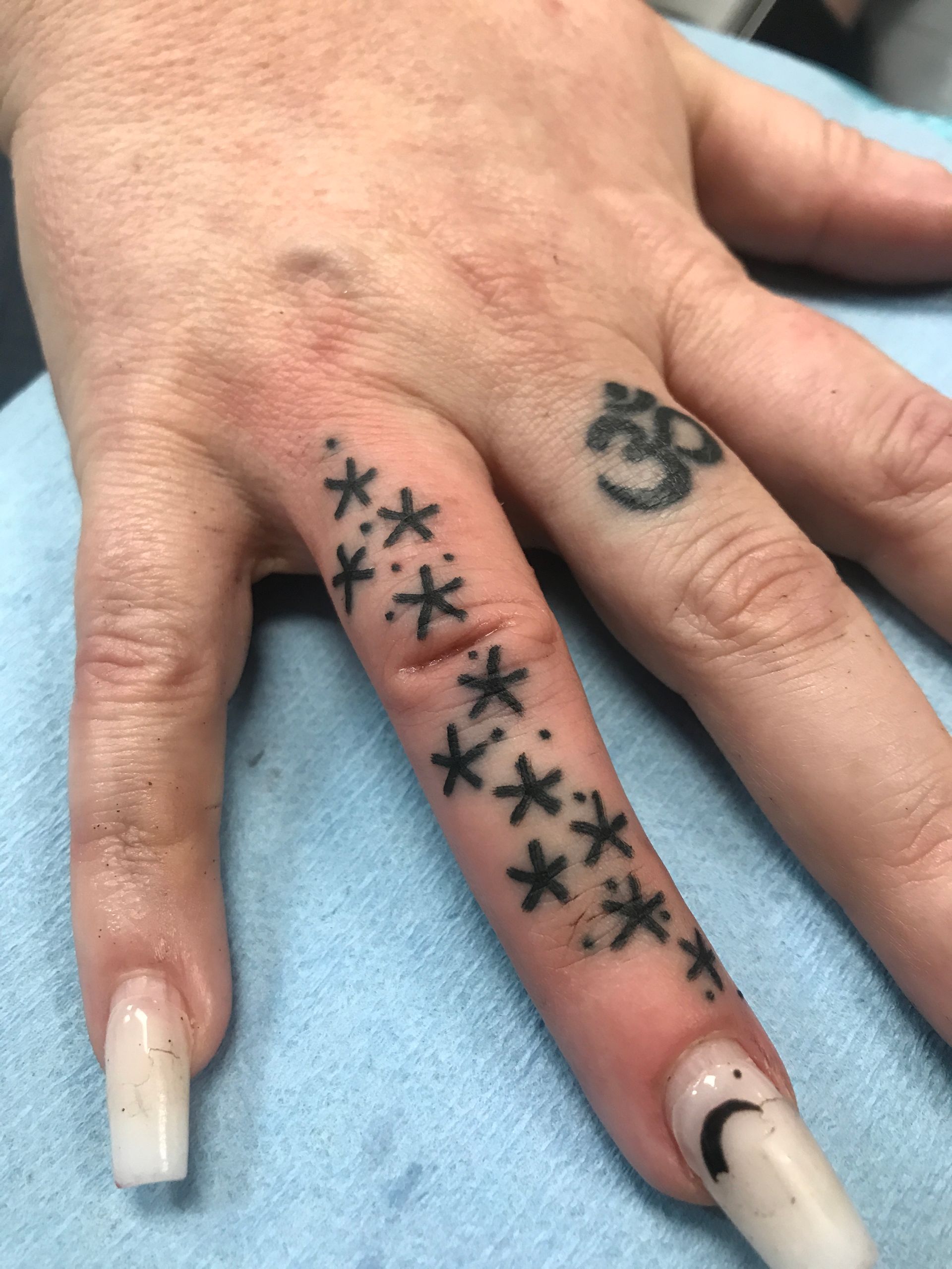 Hand with finger tattoos of asterisks and Om symbol. Long nails with glitter.