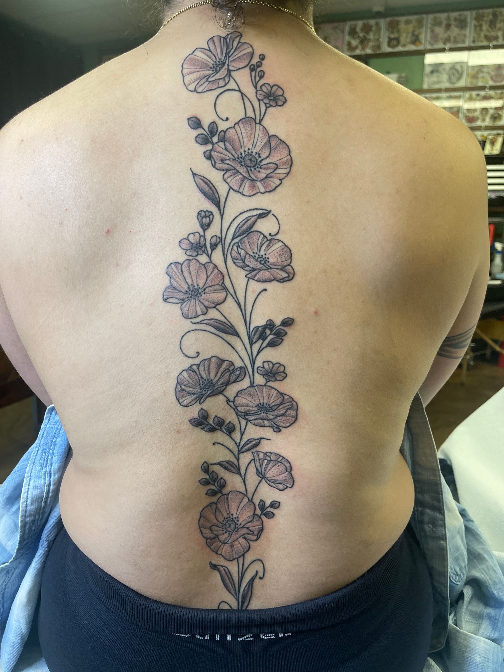 Floral tattoo down a person's spine. Pale pink and dark gray blooms with green stems and leaves.