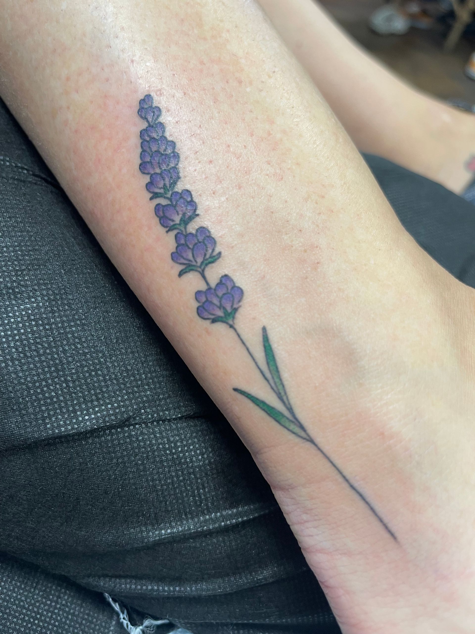 Lavender flower tattoo on a forearm, purple and green against pale skin.
