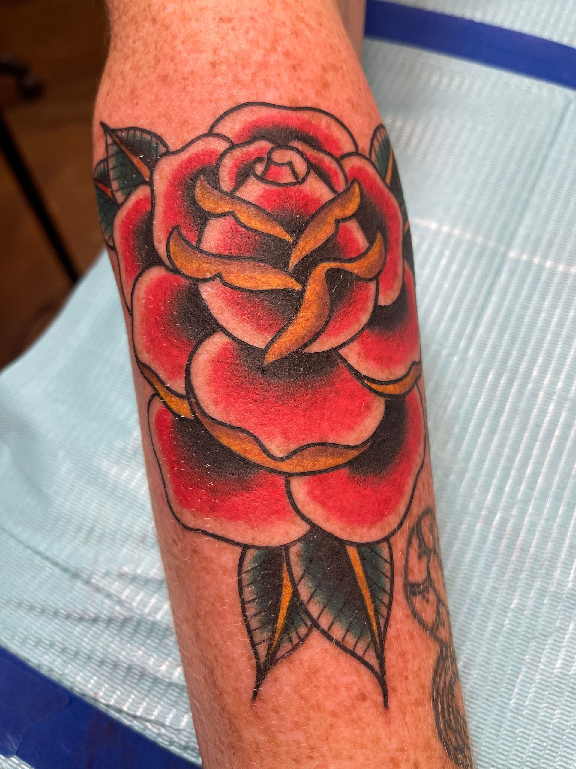 Tattoo of a red rose with black and yellow details on a person's arm.
