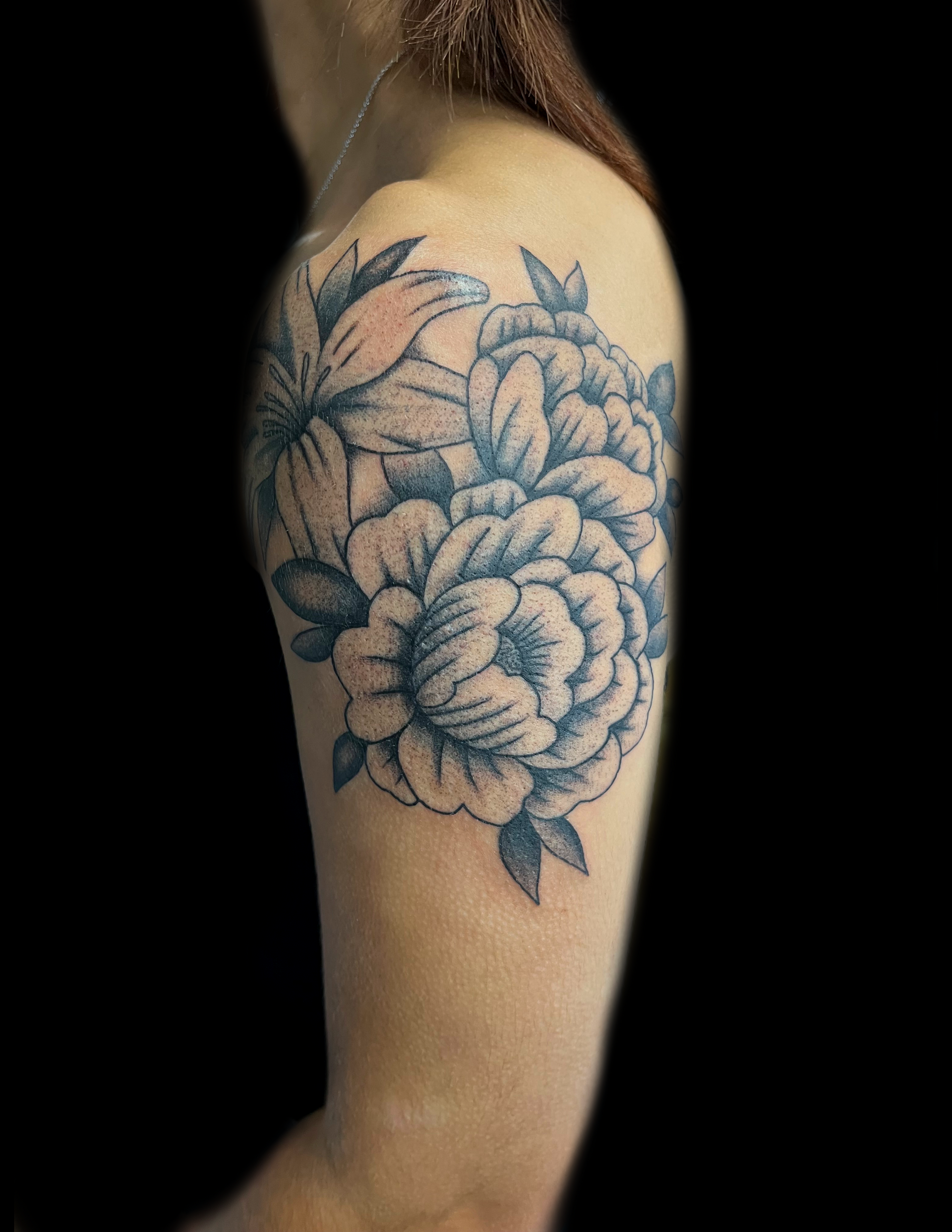 Floral tattoo on upper arm; large peony with leaves, lily in soft blue and white.