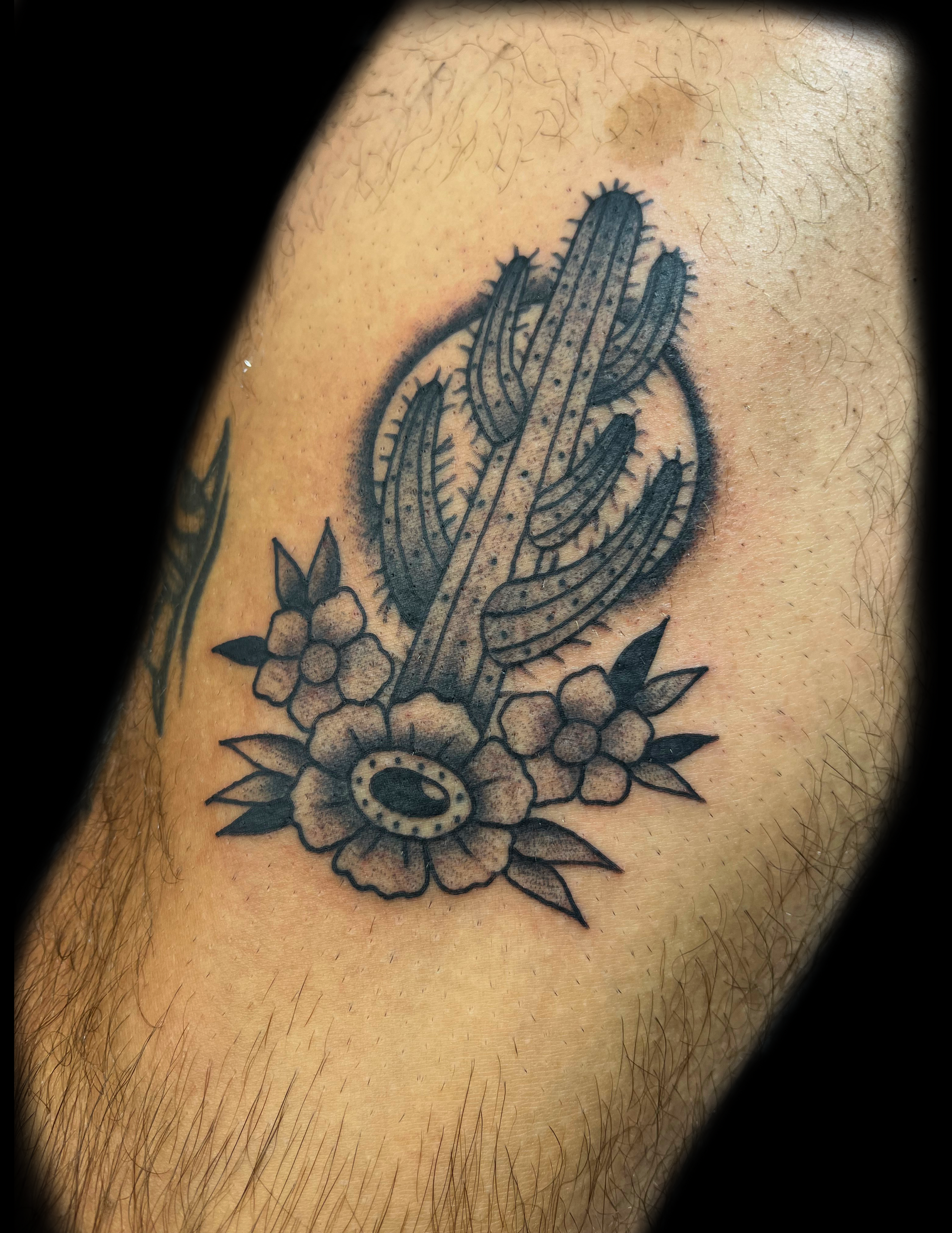 Black tattoo of a cactus, surrounded by flowers, on a person's arm.