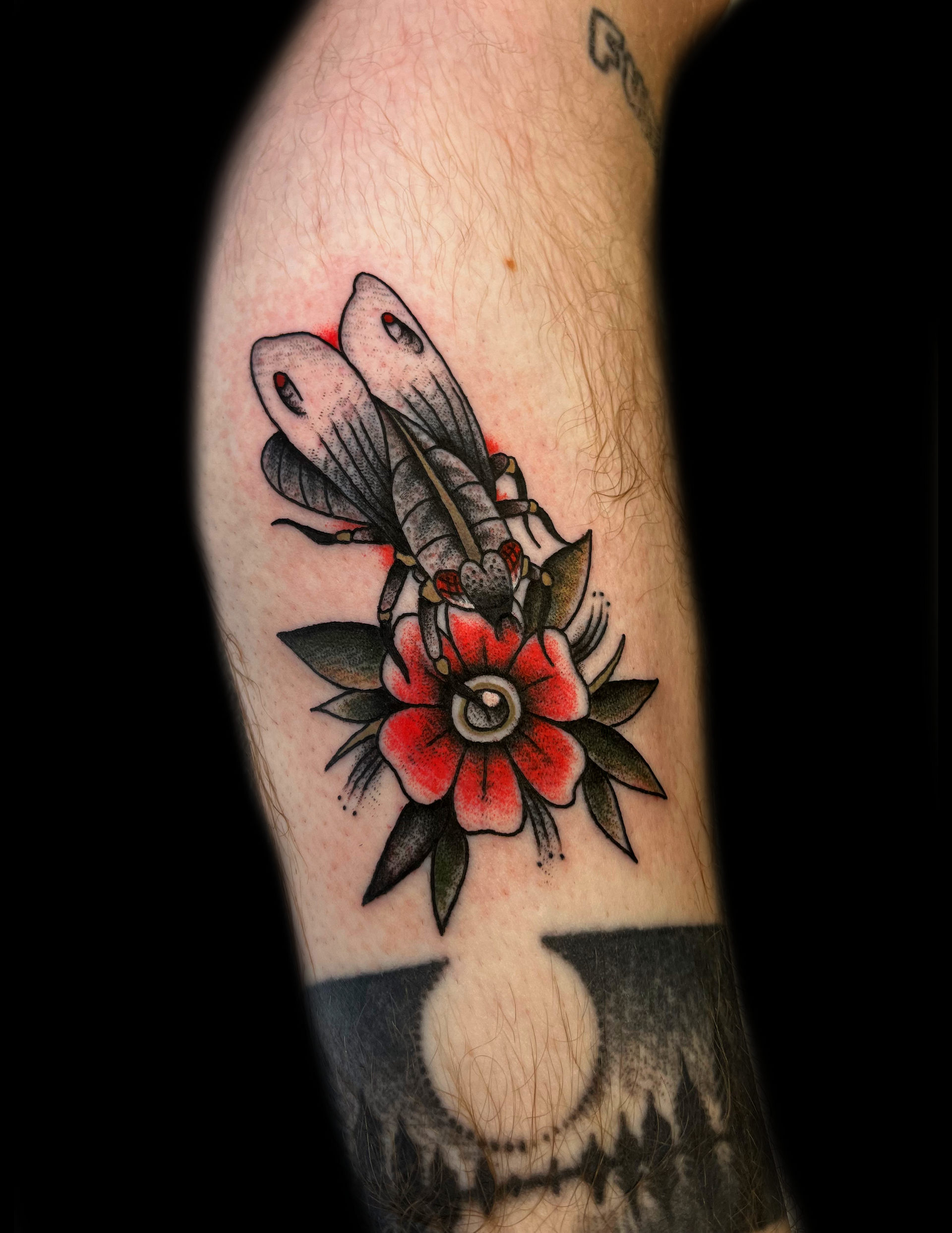 Tattoo of a dragonfly and a red flower with an eye in the center, on a person's arm.