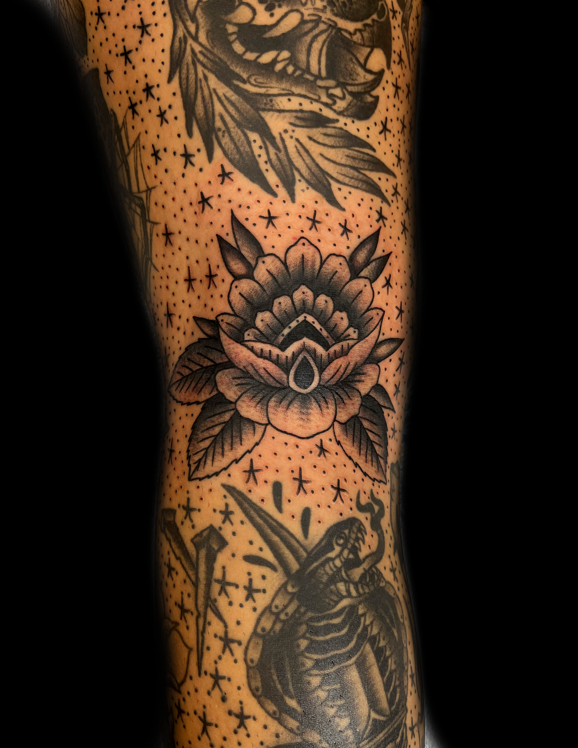 Black ink tattoo of a flower, leaves, stars, and other illustrations on skin.