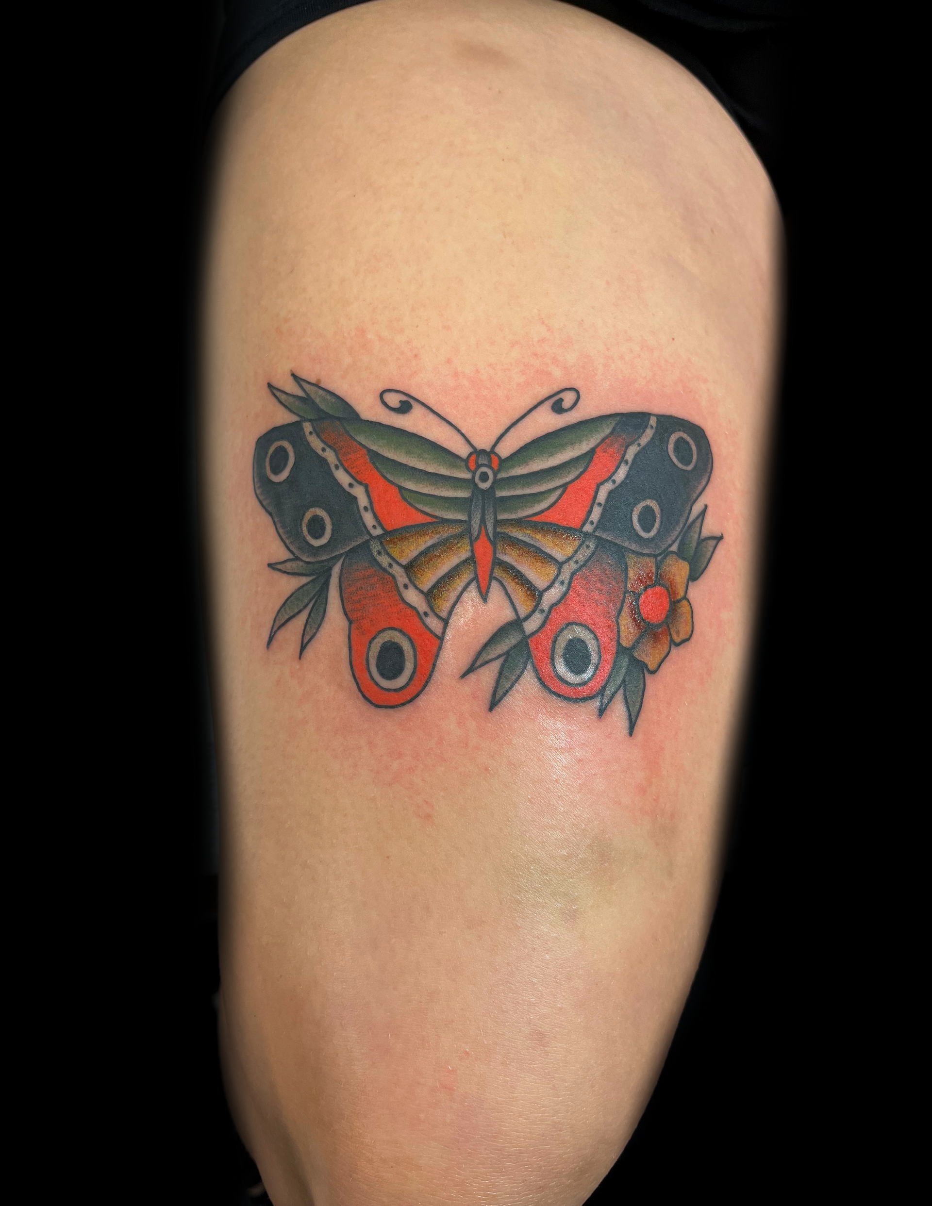 Butterfly tattoo on a light-skinned arm; red, black, green, and yellow wings with floral accents.