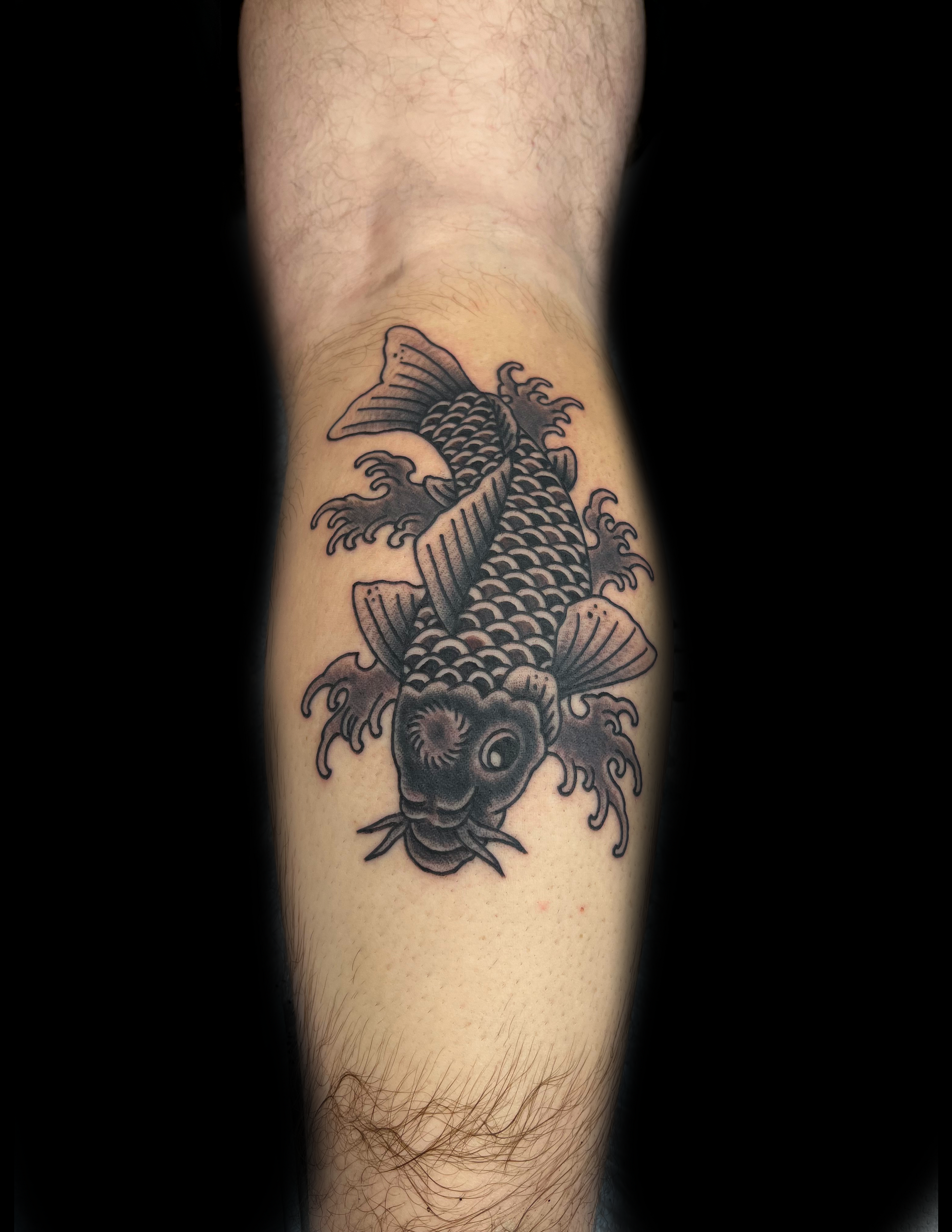 Black and gray koi fish tattoo on a person's leg.