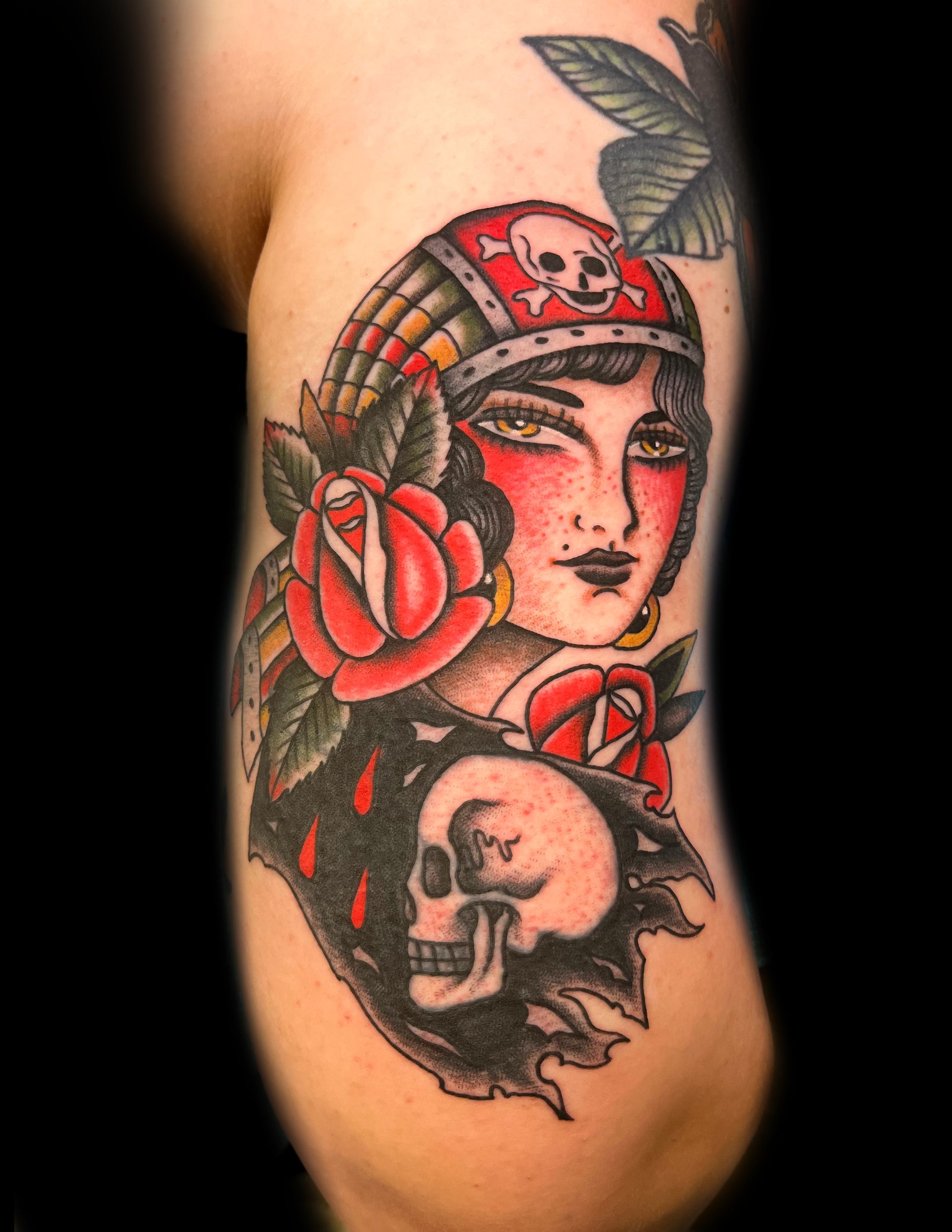 Tattoo of a woman in a skull-adorned headdress, surrounded by roses and a skull over flames.
