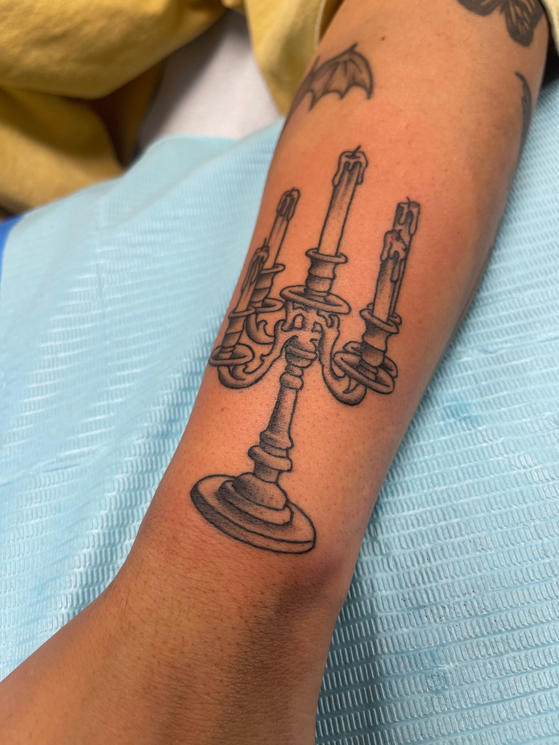 Arm with a tattoo of a three-branched candelabra with lit candles in black ink.
