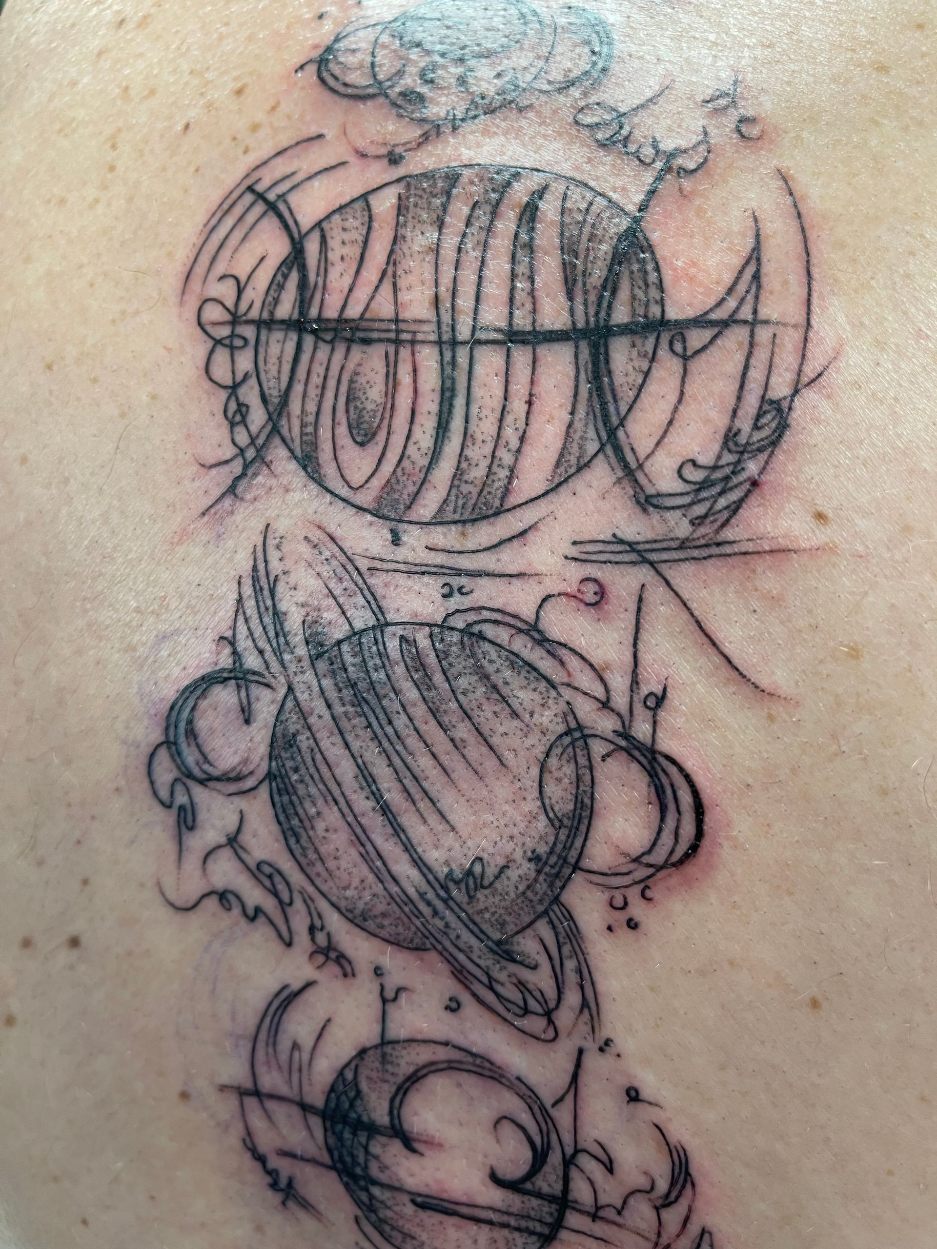 Black and white tattoo of stylized planets with swirling lines and abstract shapes.