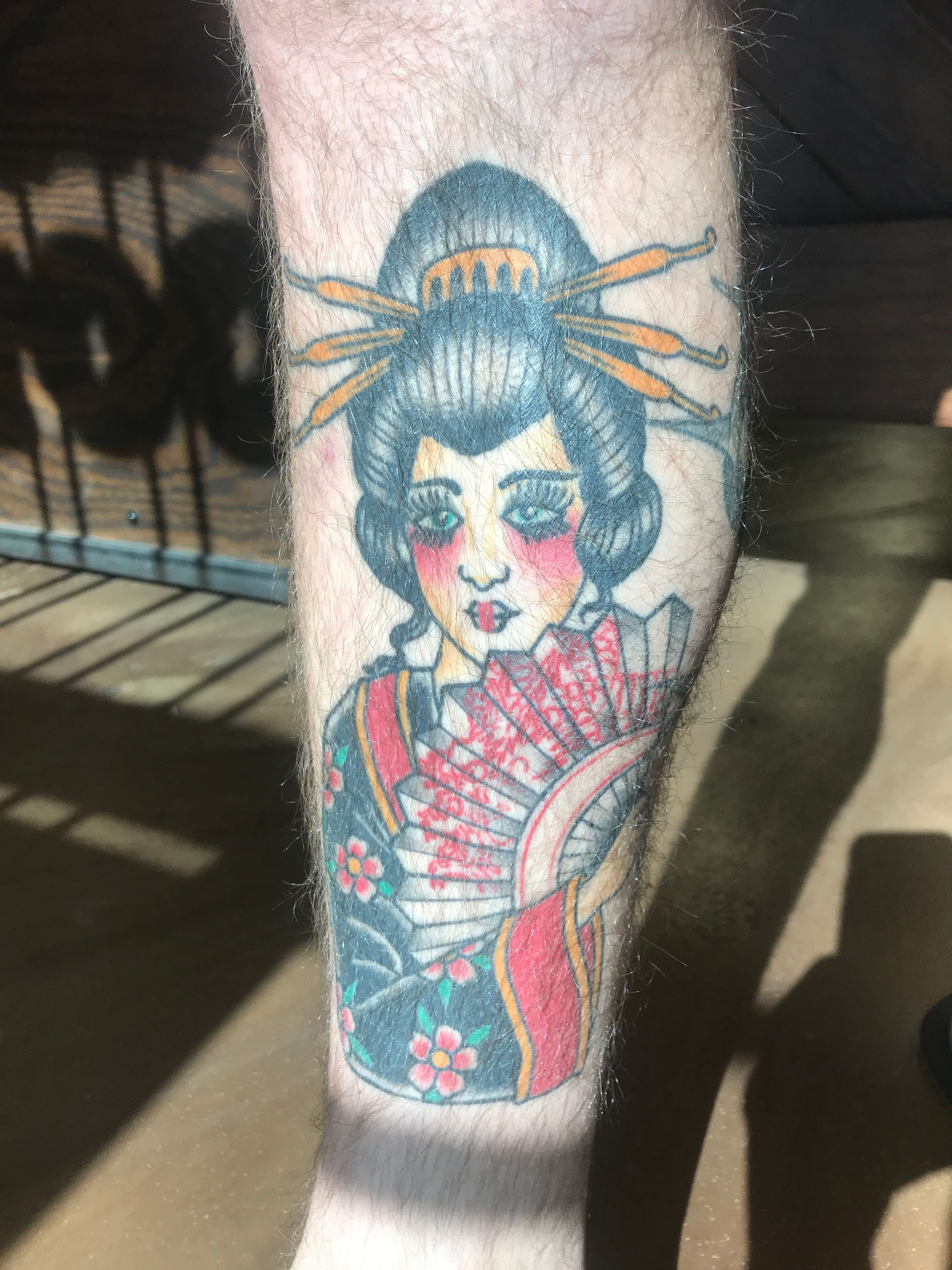 Tattoo of a geisha holding a fan, with a black and red kimono. The tattoo is on a leg.