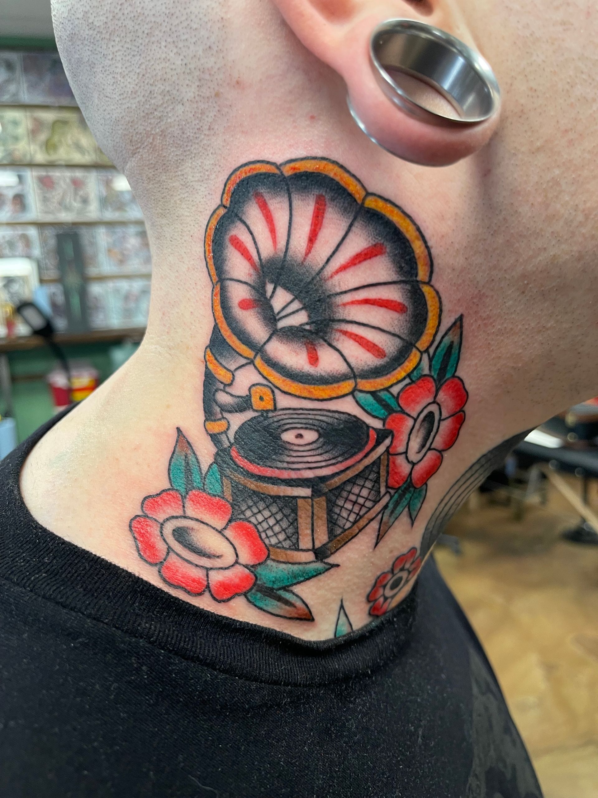 Tattoo of a vintage gramophone with flowers on a person's neck. Colorful, traditional style.