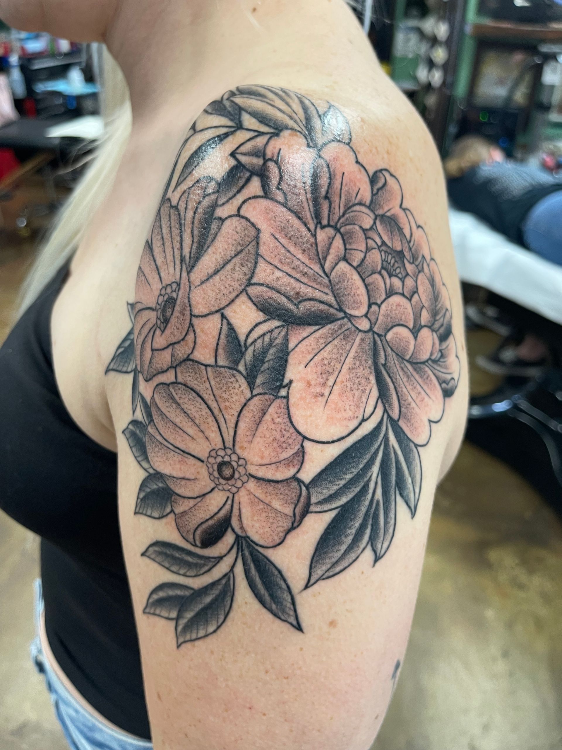 Black and grey floral tattoo on a person's shoulder, featuring a peony and other flowers.