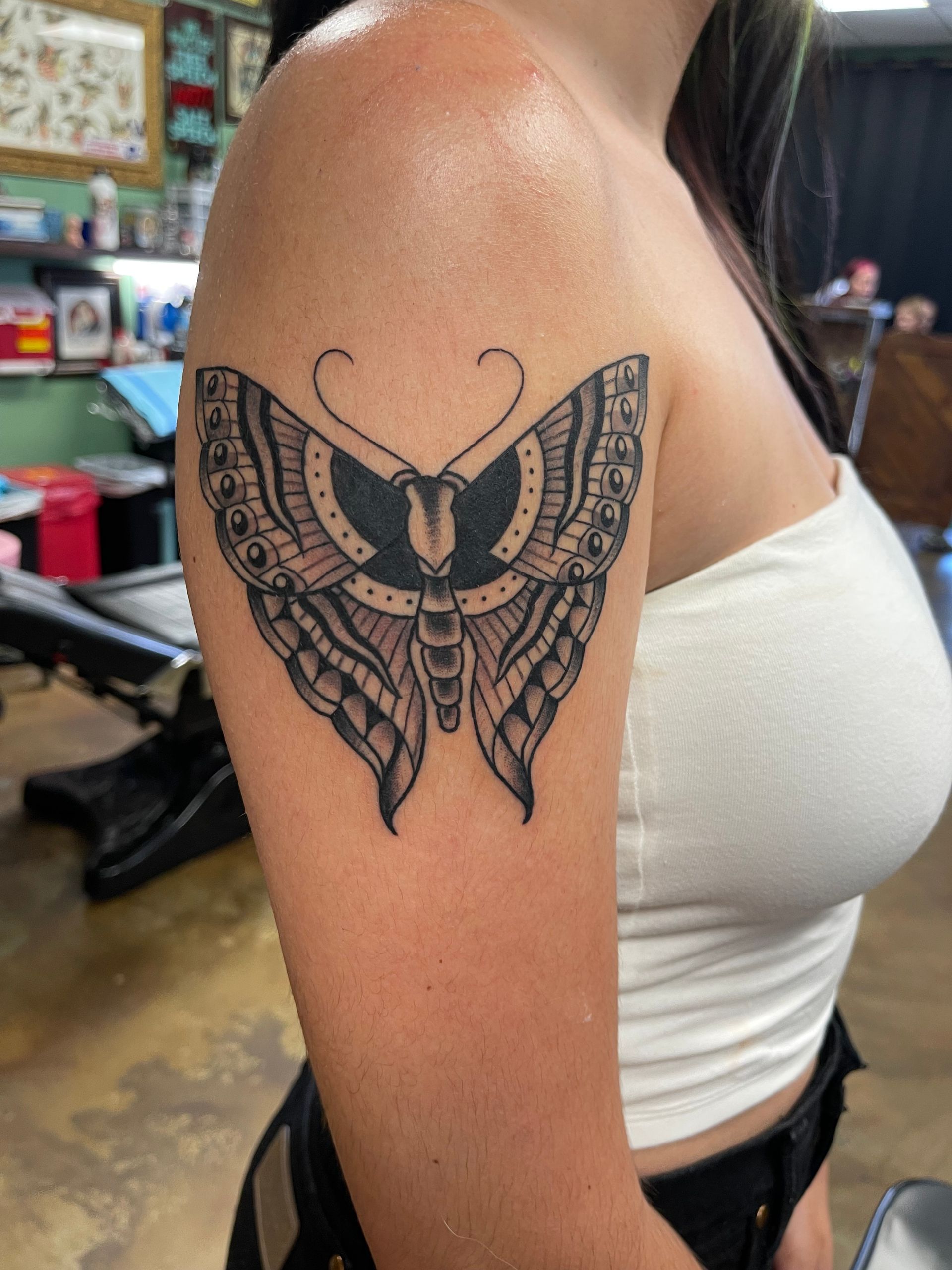 Woman's arm with a detailed black and gray butterfly tattoo on the upper arm.