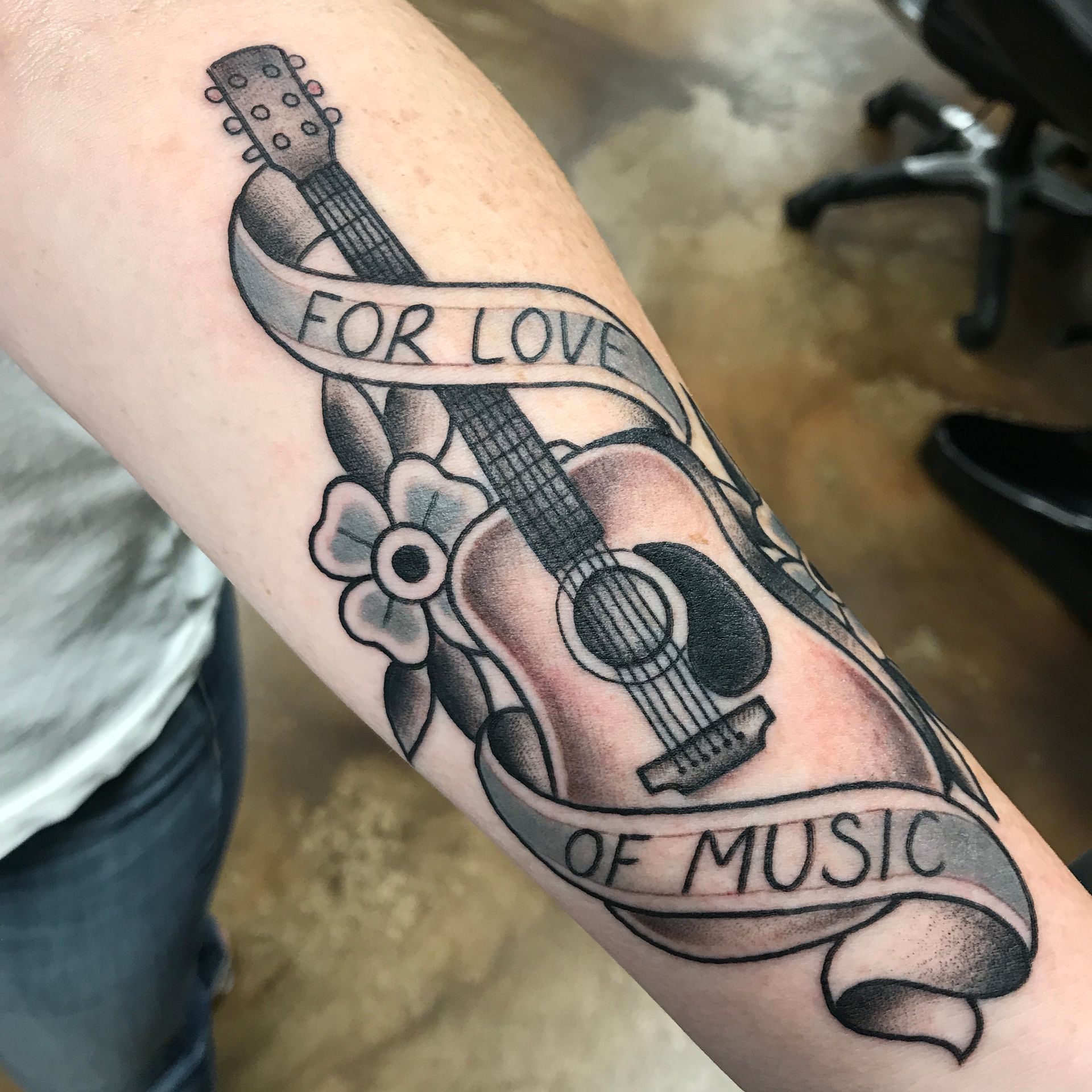 Tattoo of an acoustic guitar with a banner reading 