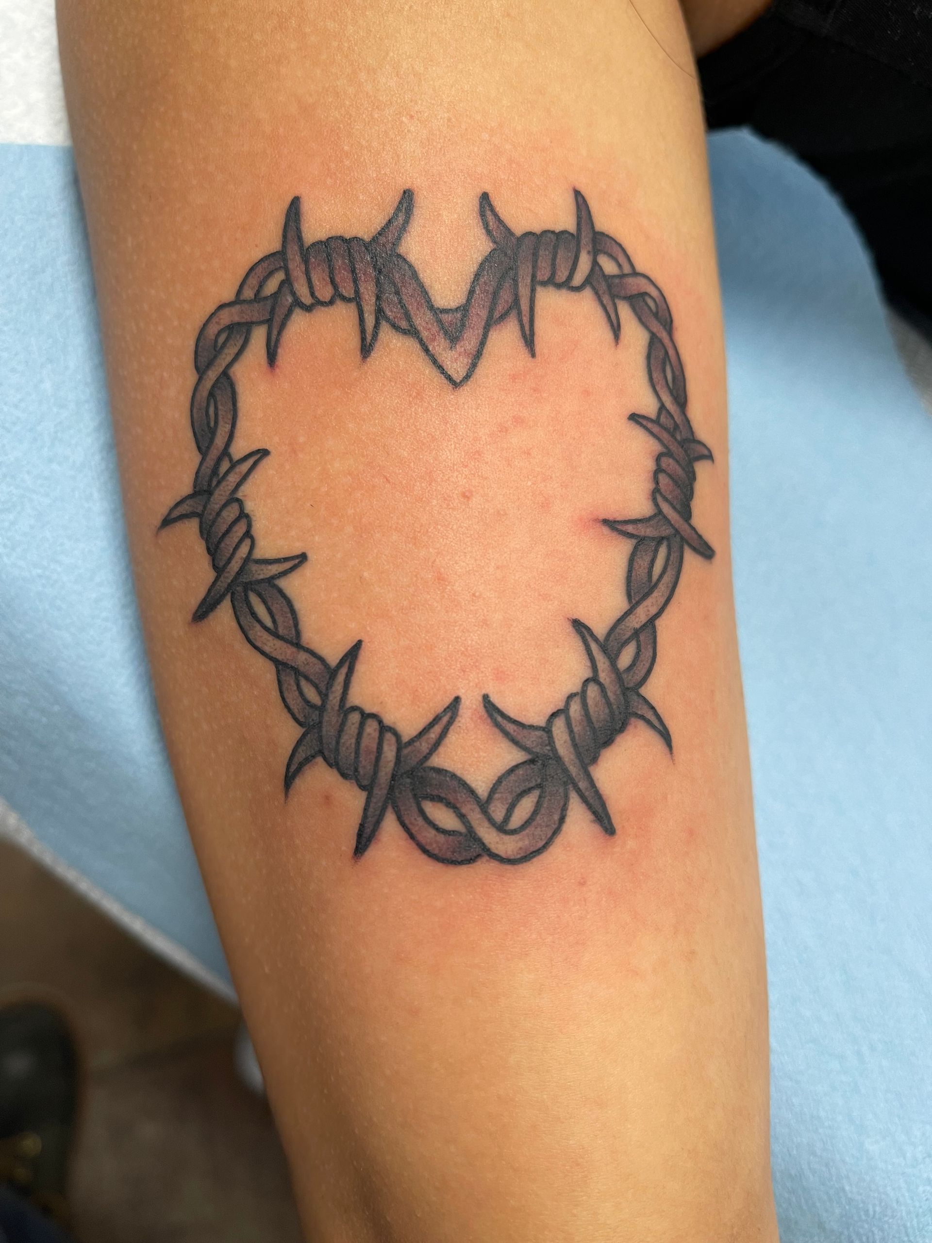 Tattoo of a heart shape made of barbed wire on a person's arm.