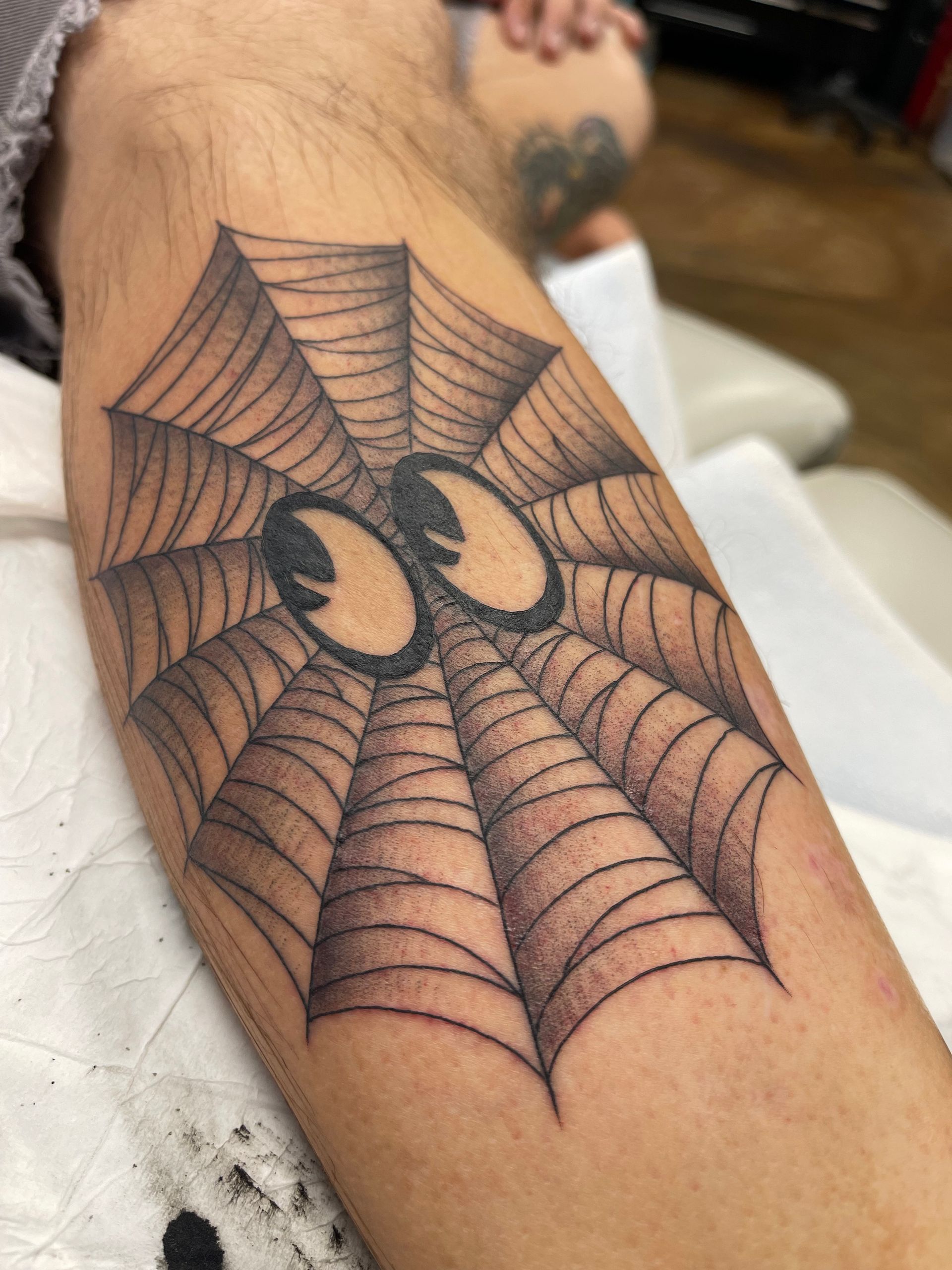Tattoo of a spiderweb with cartoon eyes on a person's leg.